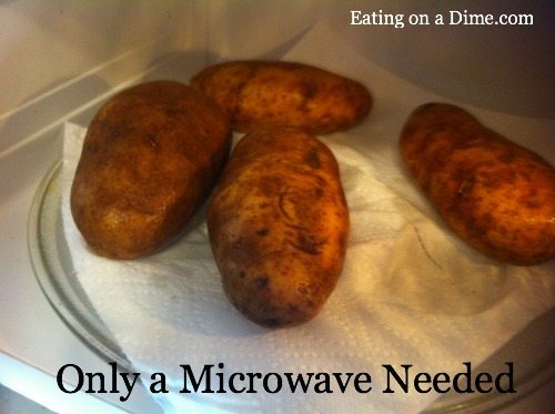 Close up image of 4 large potatoes on a paper towel in the microwave.