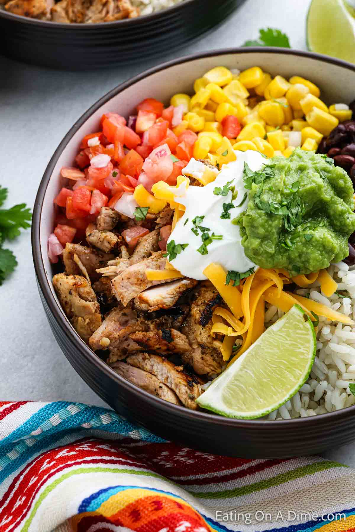 Grilled chicken in a bowl with diced tomatoes, corn, black beans and rice topped with guacamole and sour cream with shredded cheese