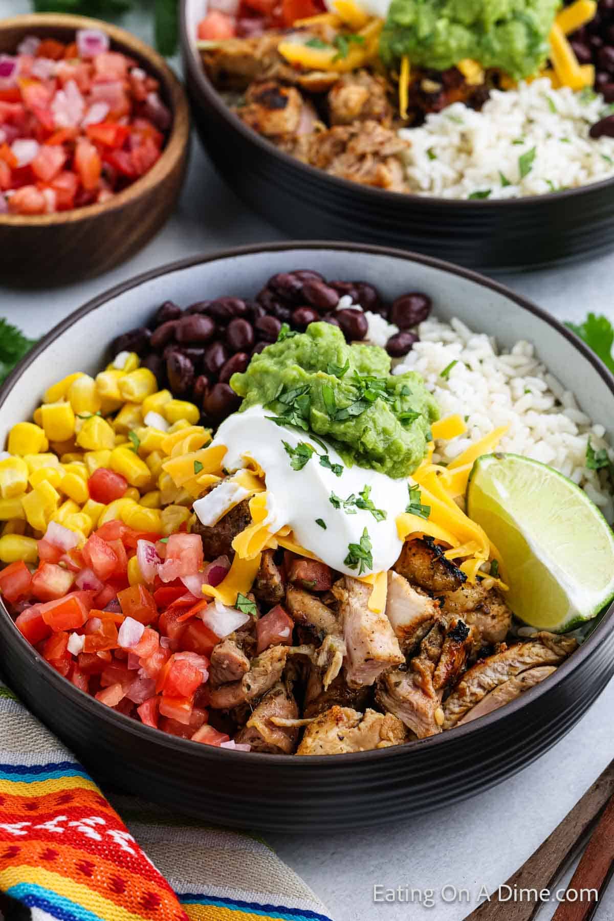 Grilled chicken in a bowl with diced tomatoes, corn, black beans and rice topped with guacamole and sour cream with shredded cheese