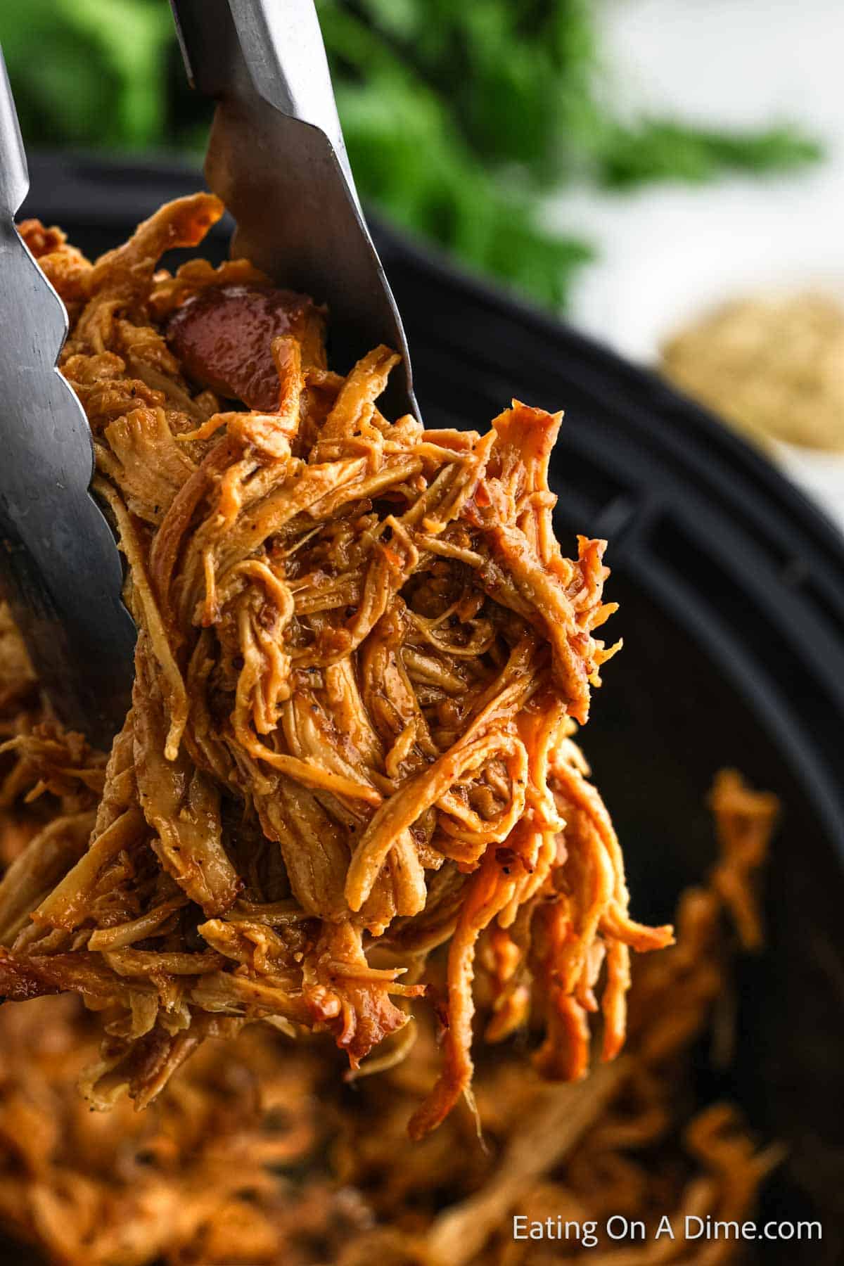 Shredded honey mustard chicken in the slow cooker with a serving on tongs