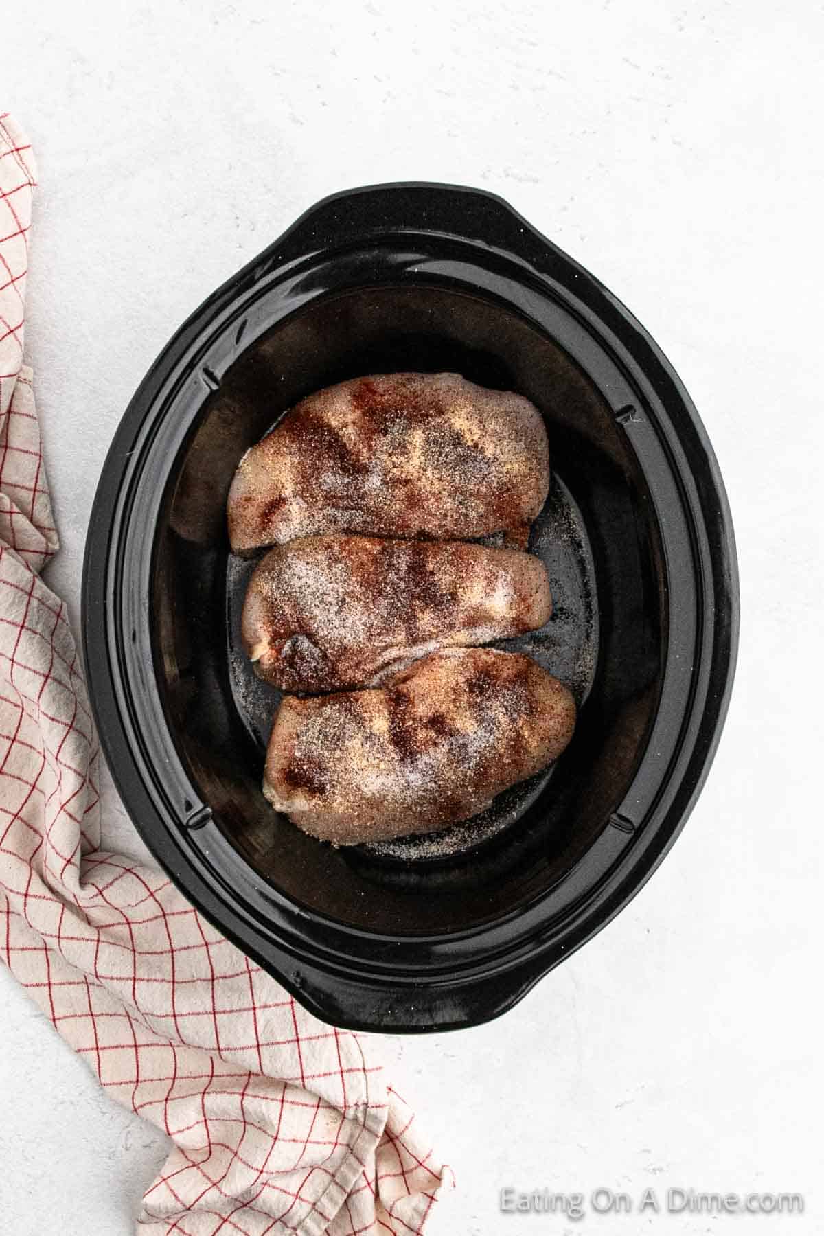 Placing chicken breast in the slow cooker topped with seasoning