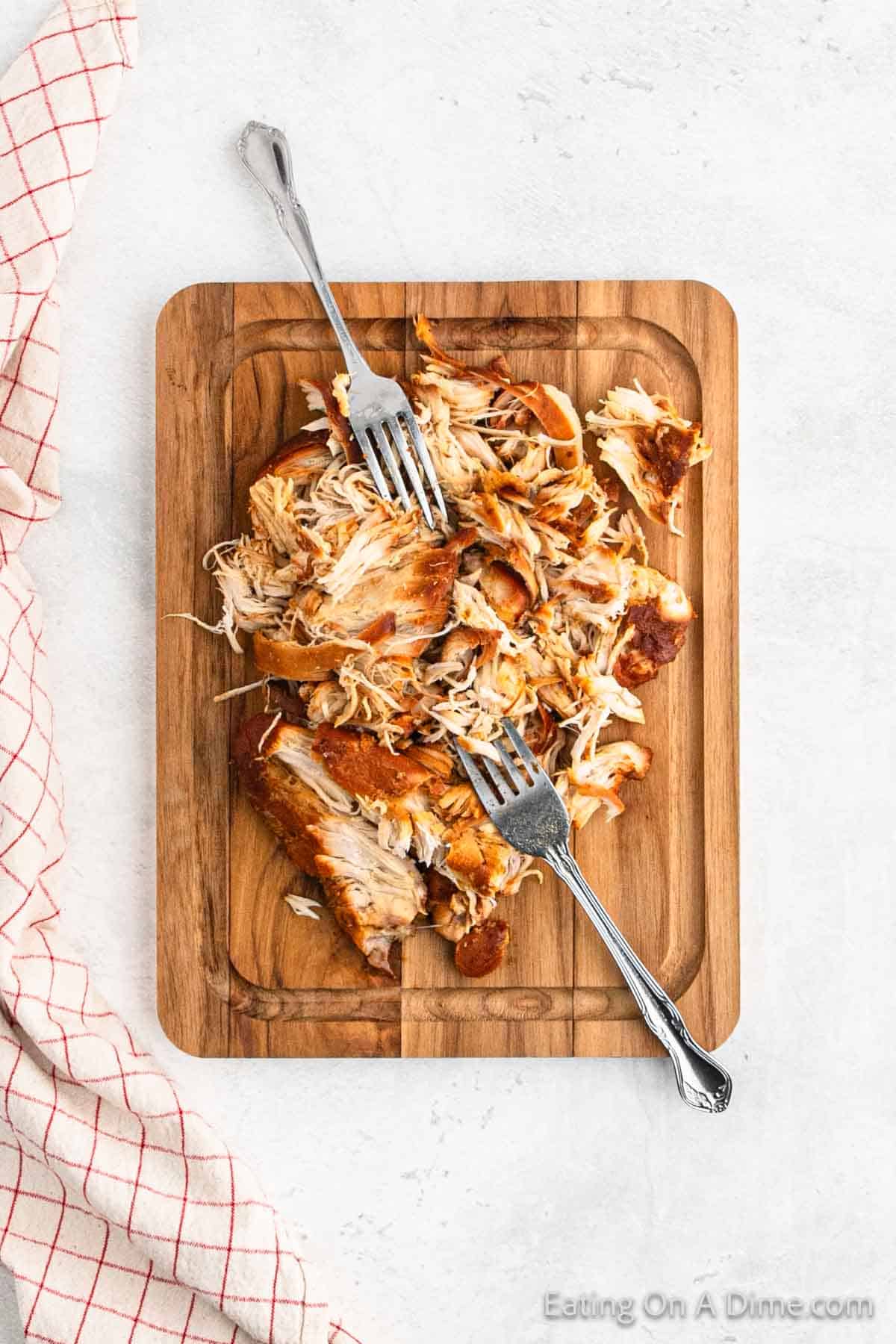 Shredding chicken on a cutting board with two forks