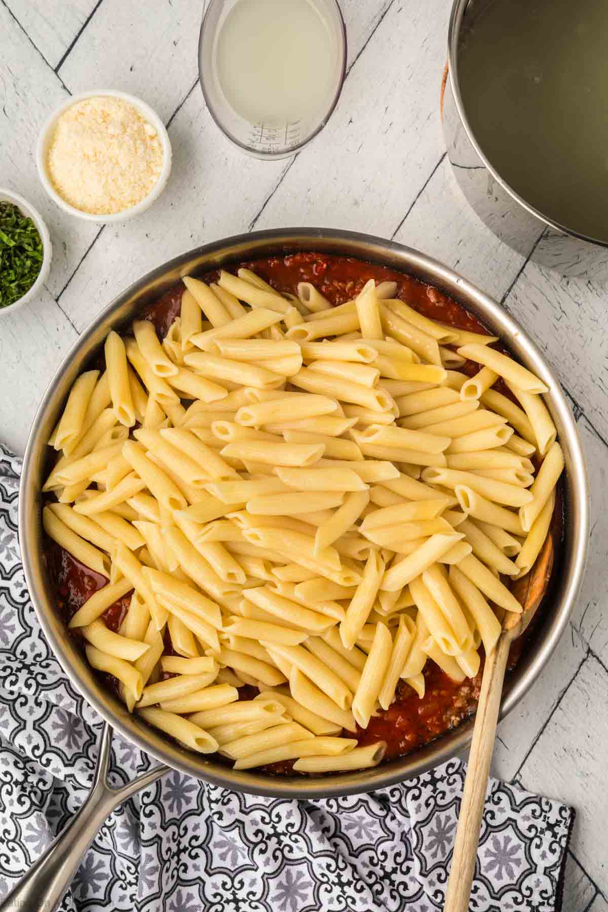 Mixing the cooked pasta with the meat sauce in a large skillet