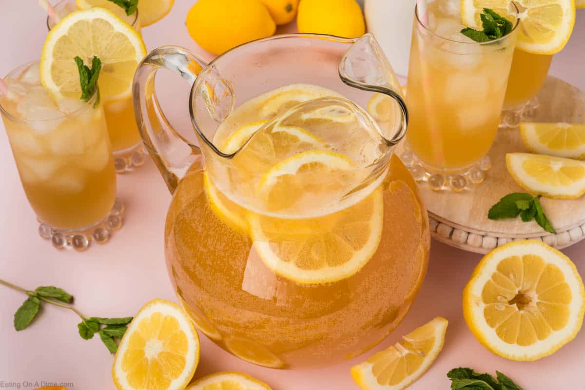Glass pitcher full of lemonade with lemon slices and glasses of lemonade 