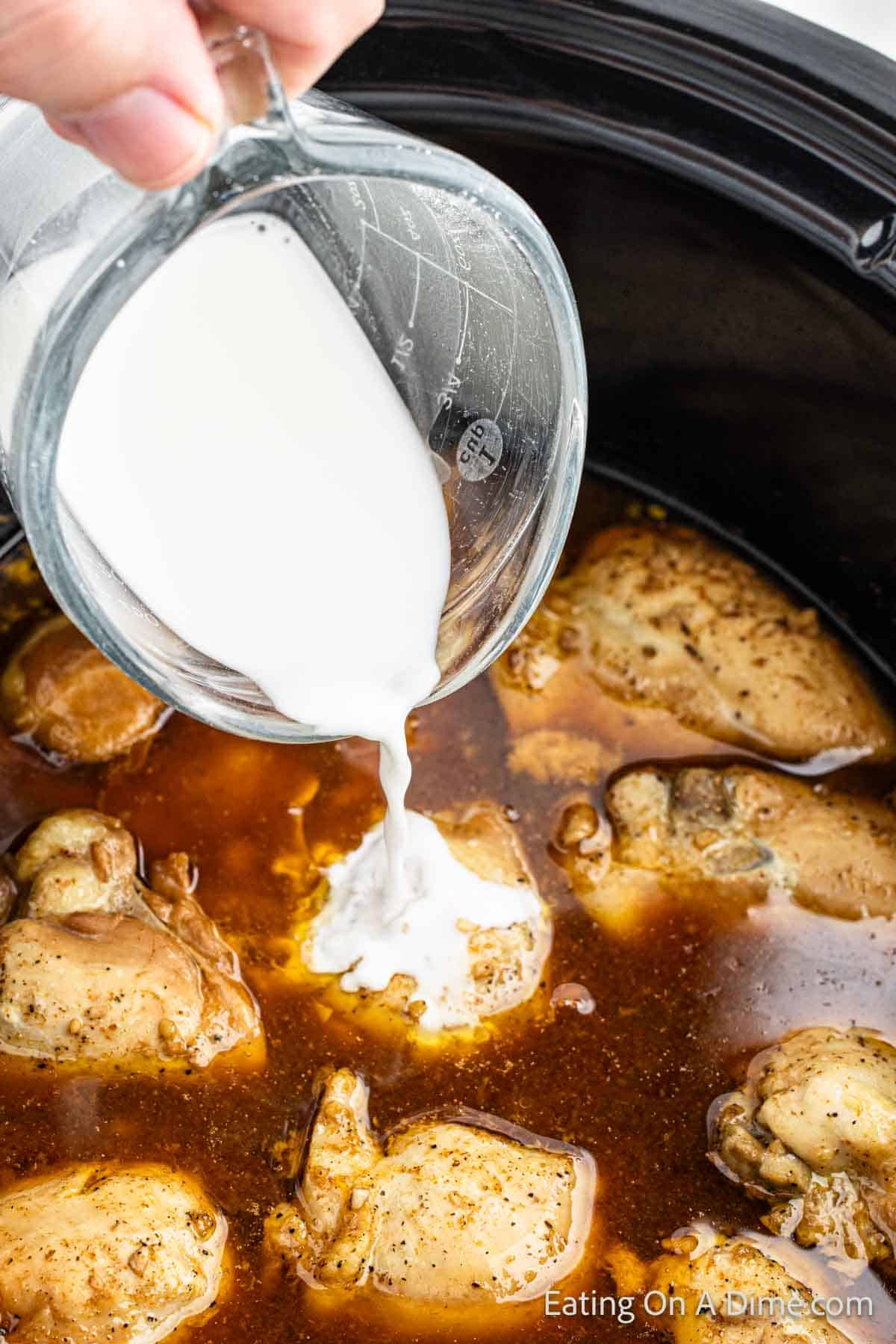 Pouring the heavy cream over the chicken thighs in sauce in the slow cooker