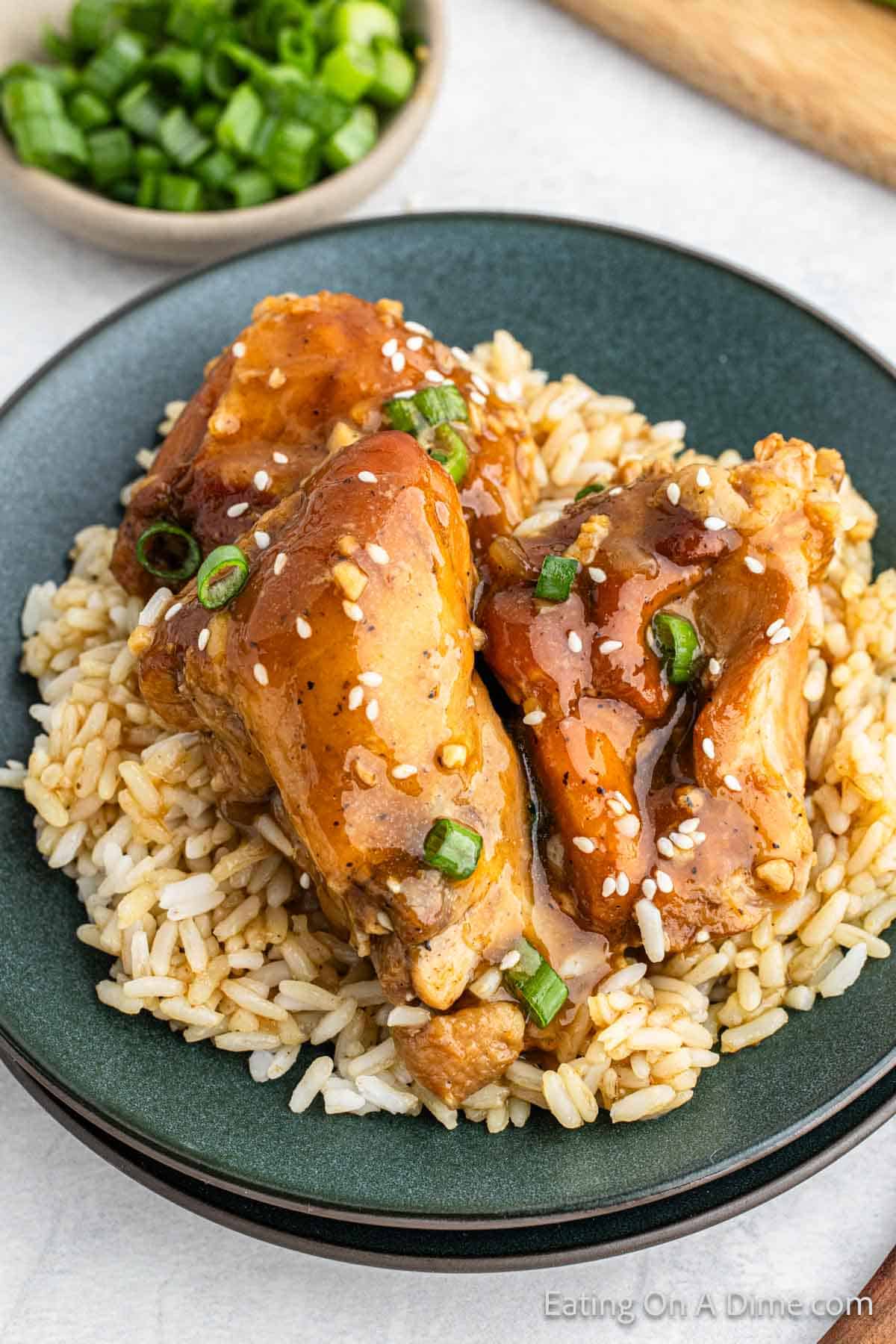Sticky Chicken served over white on a plate topped with green onions and sesame seeds