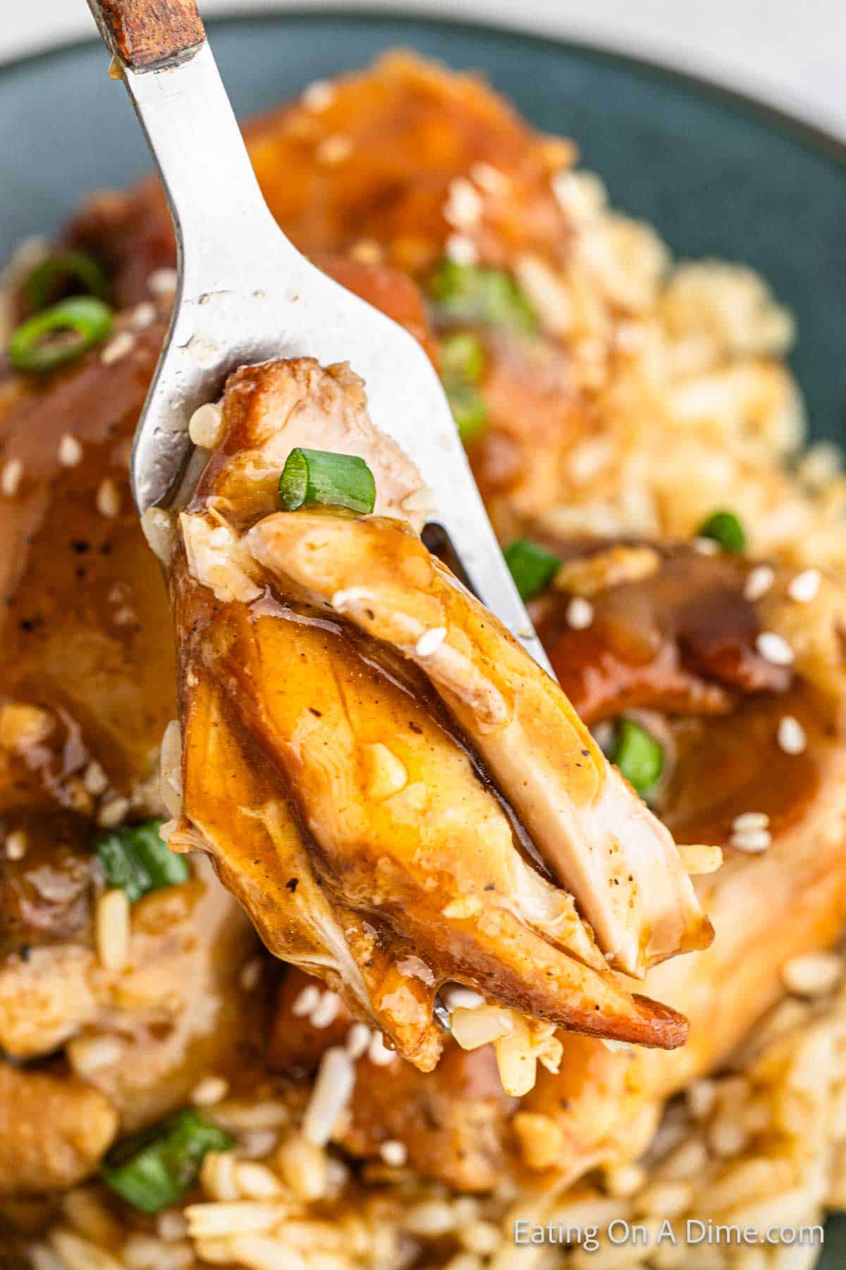 Sticky chicken in the back ground with a bite of chicken covered in sauce on a fork