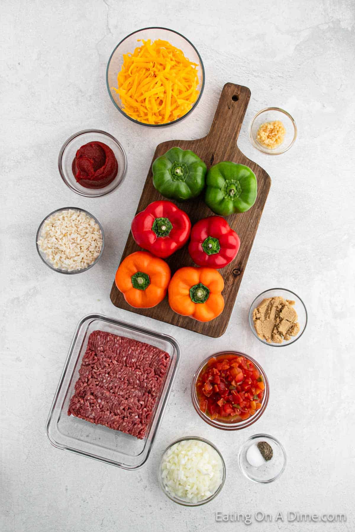 Ingredients - bowl of shredded cheese, tomato paste, rice, green, red, orange bell peppers, minced garlic, brown sugar, ground beef, diced tomatoes with green chilies, diced onions, salt, pepper