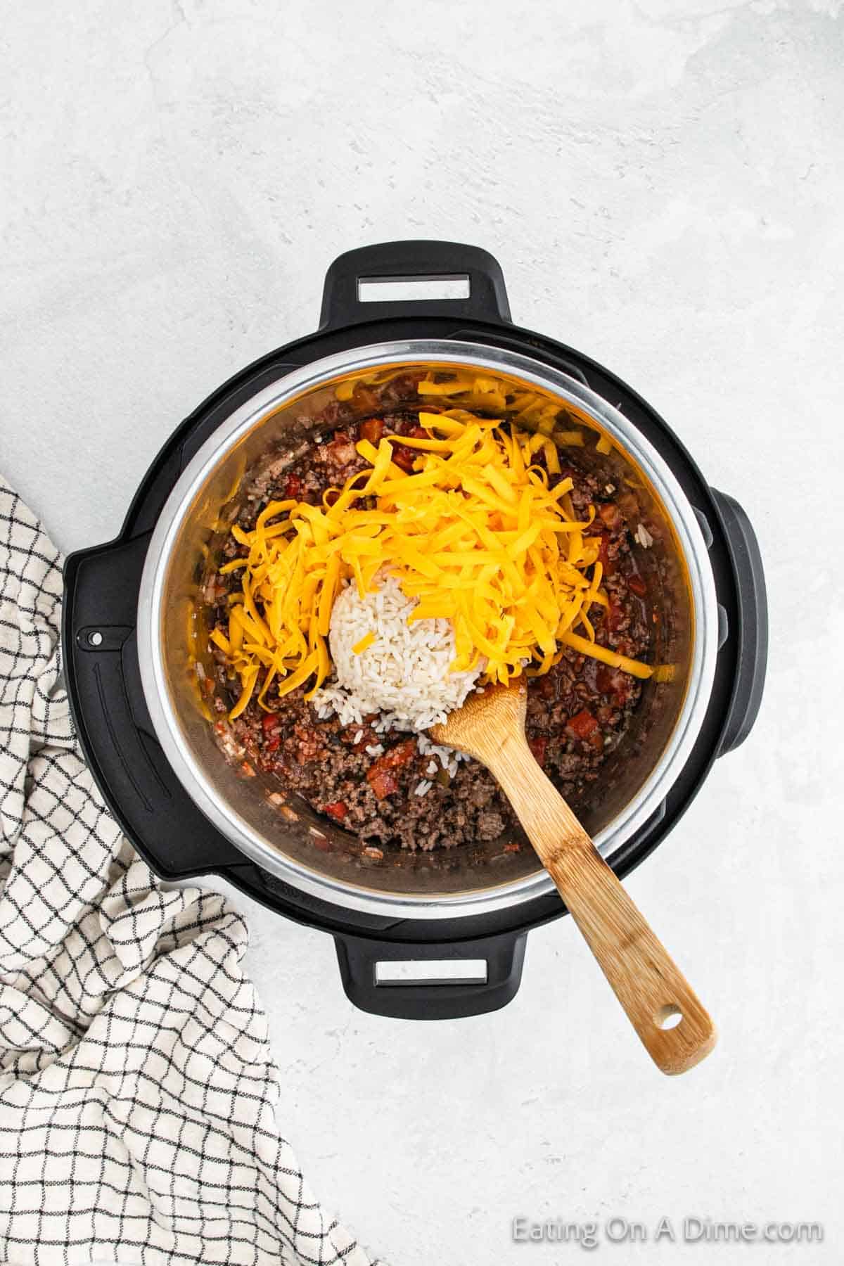 Ground beef mixture in instant pot topped with rice and shredded cheese with a wooden spoon