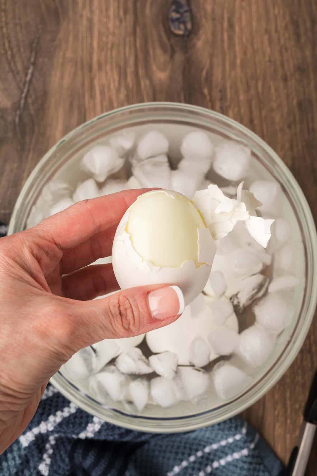 Peeled eggs being held with a bowl of ice water in the background