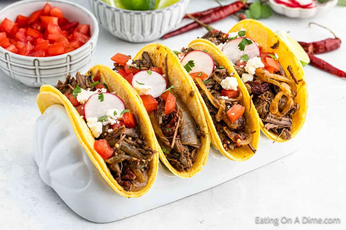 Shredded steak meat placed in corn tortillas in a taco steak in bowls of diced tomato on the side