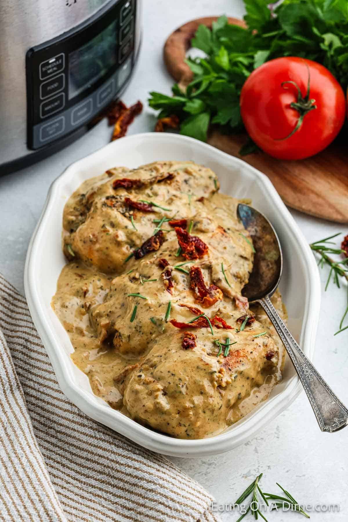 Sundried tomato chicken breast topped with creamy sauce on a platter with a silver spoon