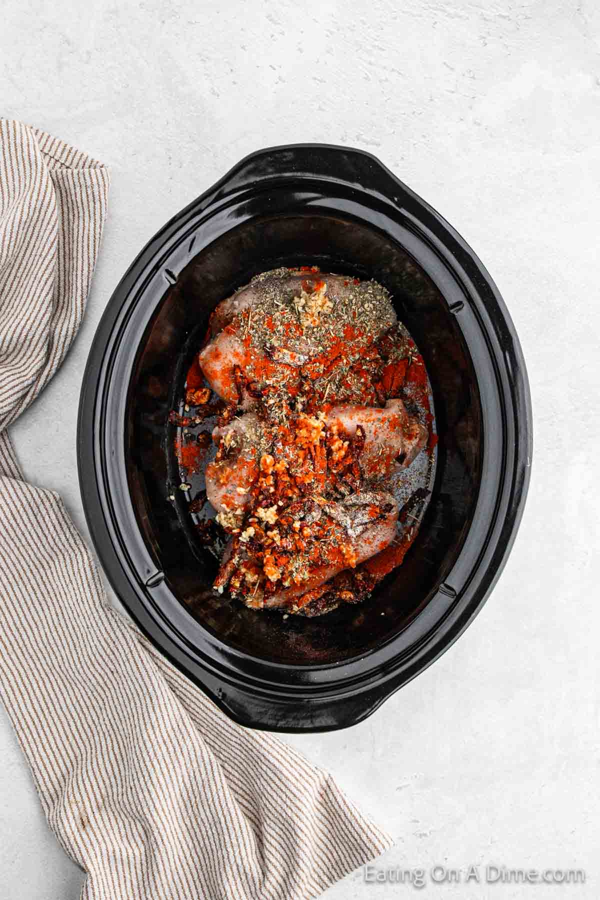 Chicken breast placed in the slow cooker topped with minced garlic, paprika, minced garlic and seasoning 