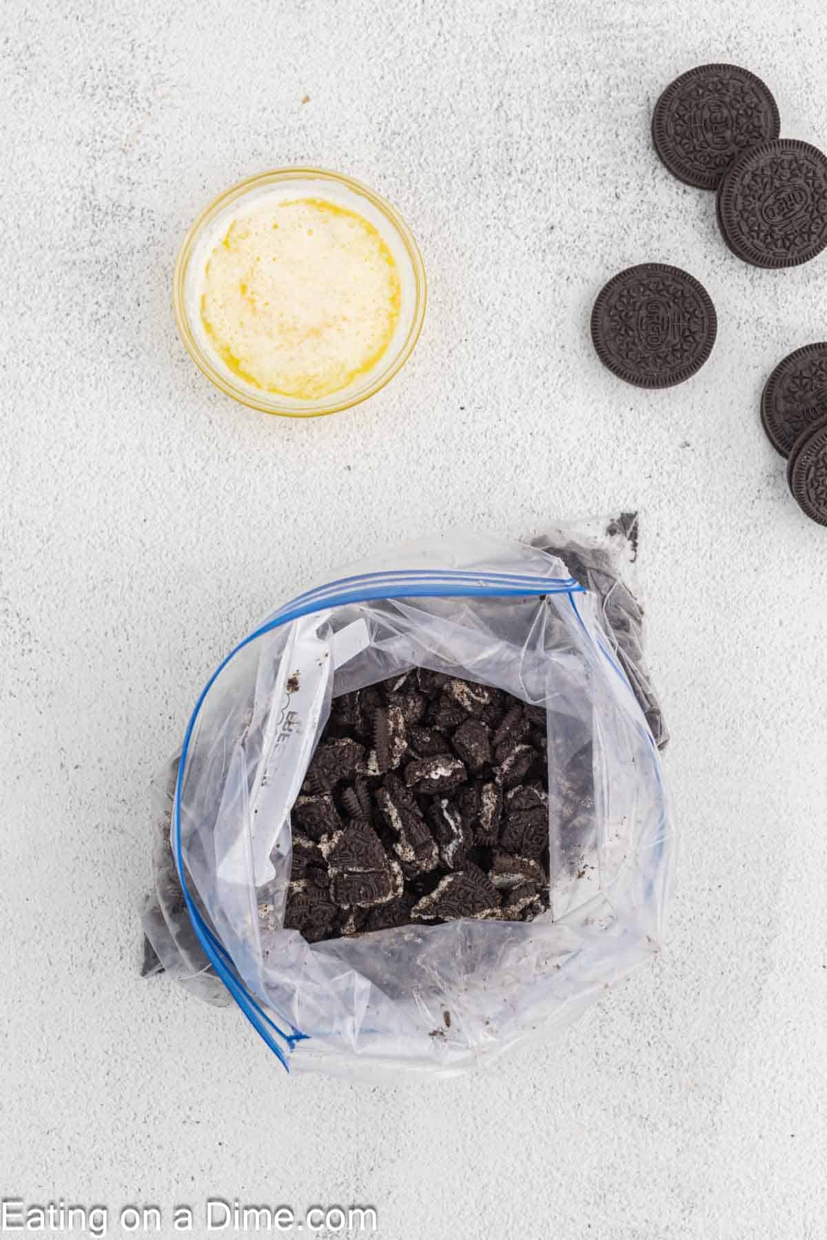 Crushed Oreos in a Zip Lock Bag with a side of Oreos and melted butter in a bowl