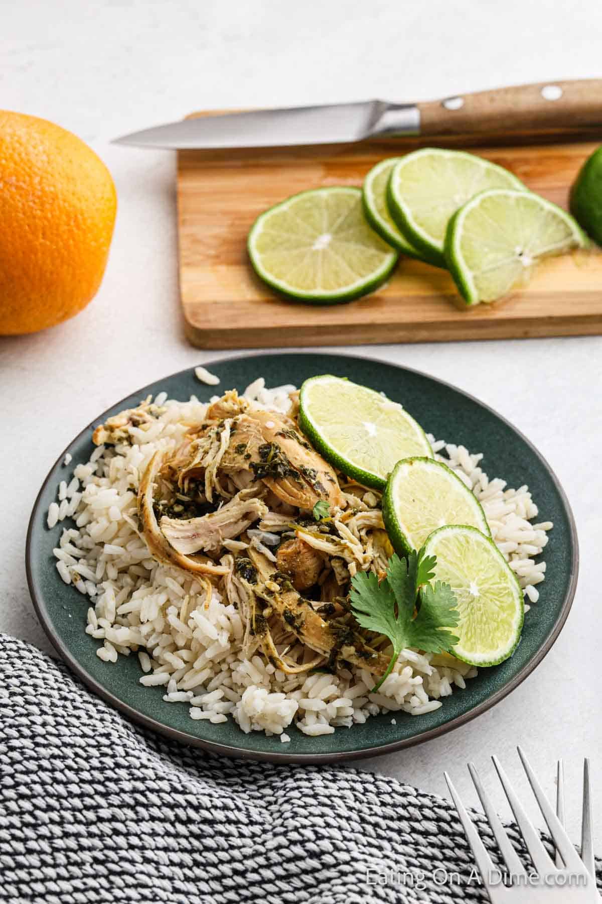 Mojo Chicken shredded topped on white rice with fresh lime slices on the side on a plate. Fresh lime slices on a cutting board on the side