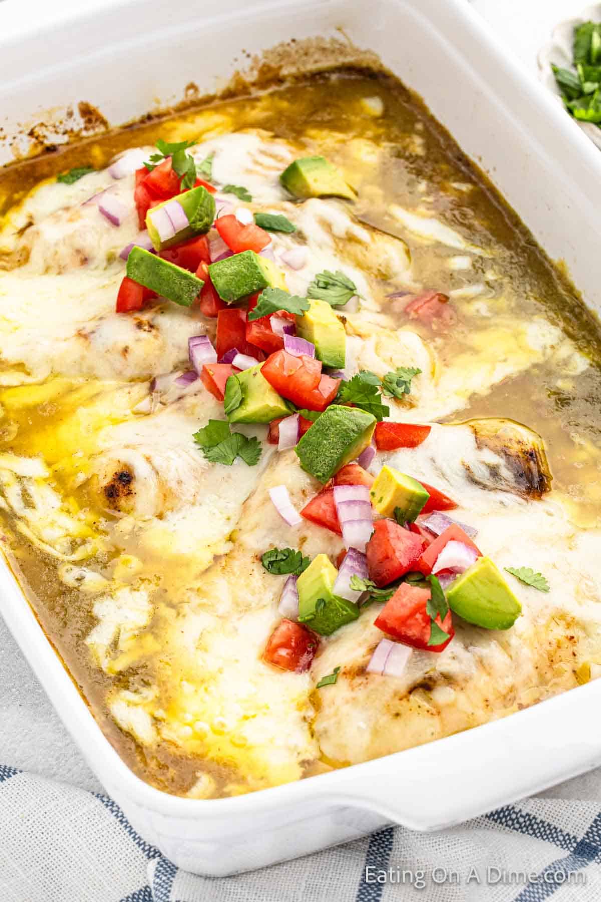 Baked Chicken Enchilada in a baking dish topped with melted cheese, diced avocado, fresh cilantro and diced tomatoes