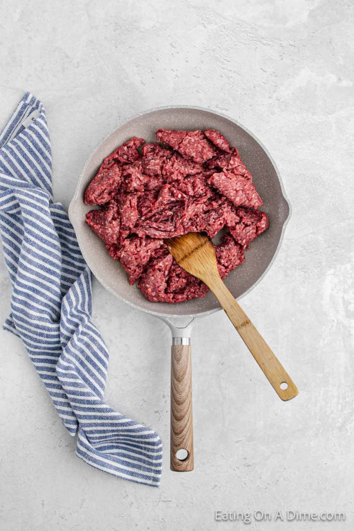 Cooking ground beef in a skillet with a wooden spoon