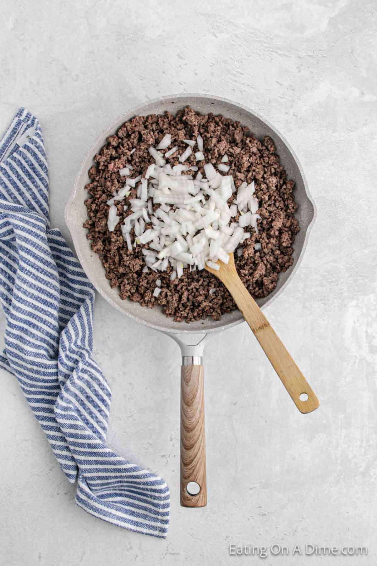 Cooked ground beef in a skillet with chopped onions with a wooden spoon