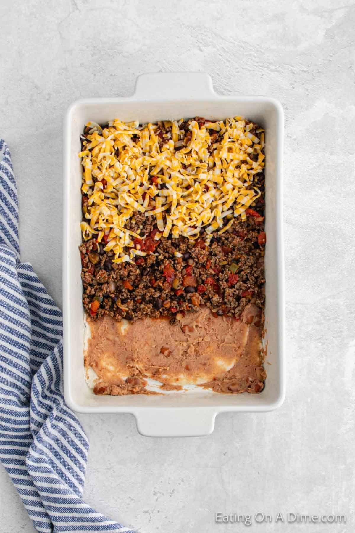 Refried beans, ground bee mixture and shredded cheese layered in a casserole dish