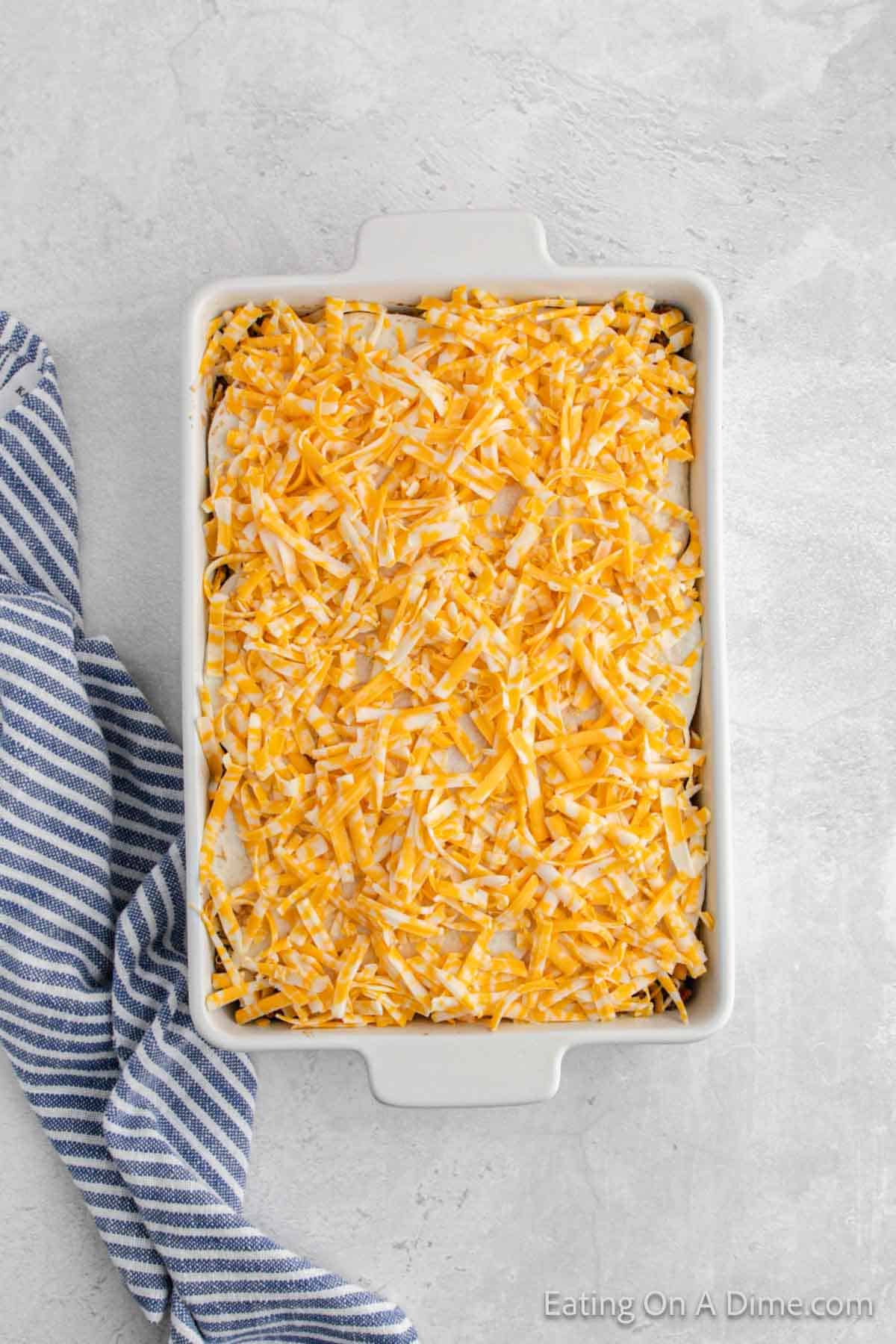 Taco lasagna topped with shredded cheese in a casserole dish