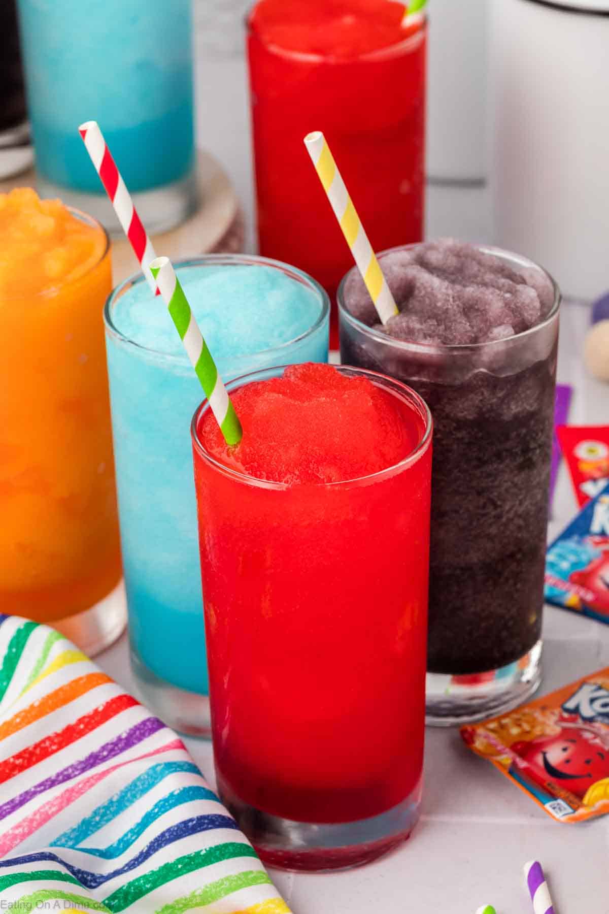 Kool Aid slushies in red, blue, purple and orange in clear glasses with stripe straws. 