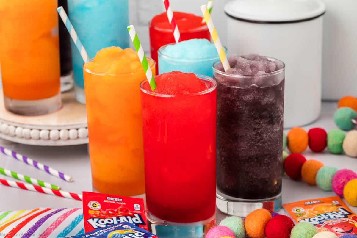 Red, orange, grape, blue slushie in clear glasses with straws