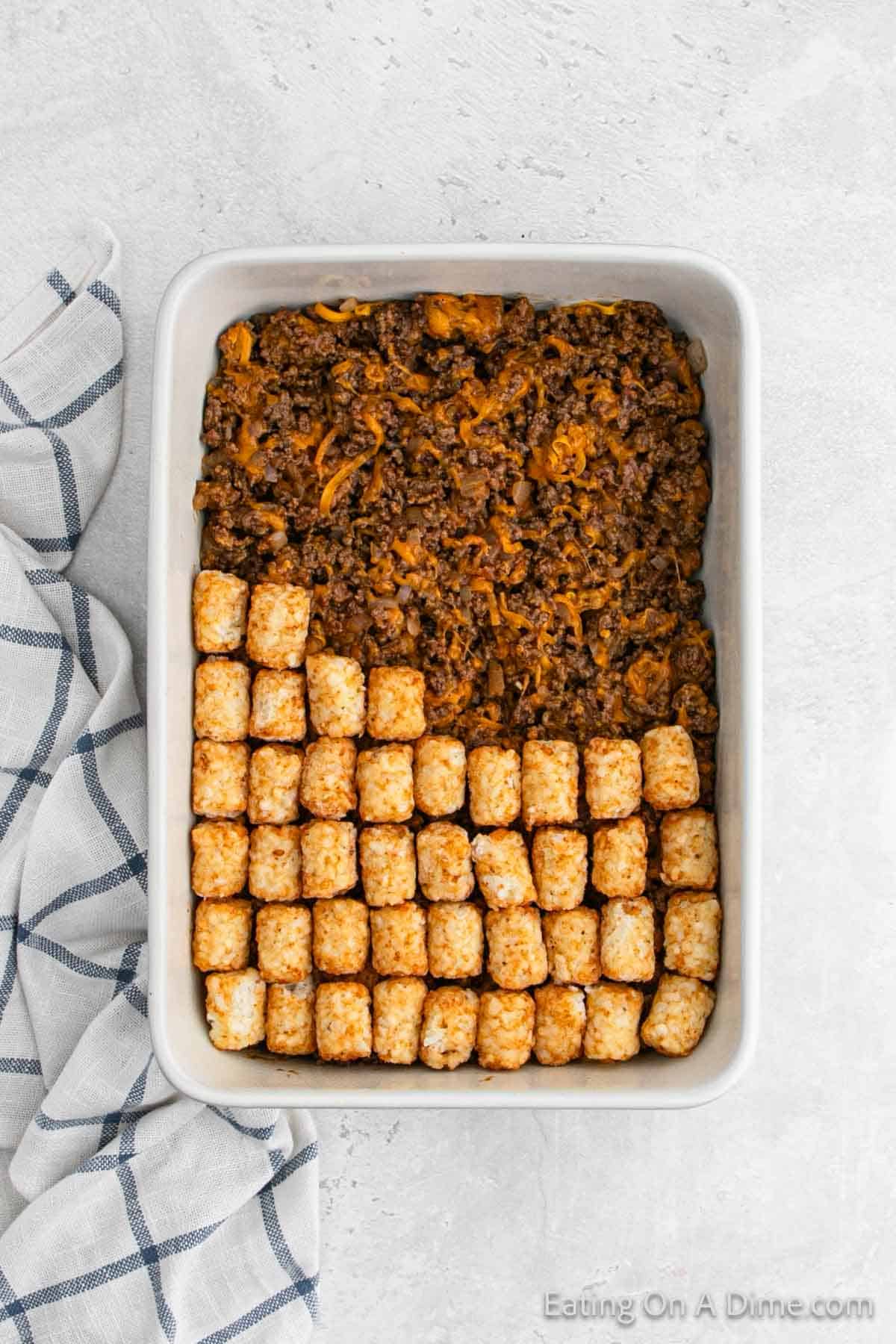 Layering ground beef mixture in a baking dish and topped with tator tots