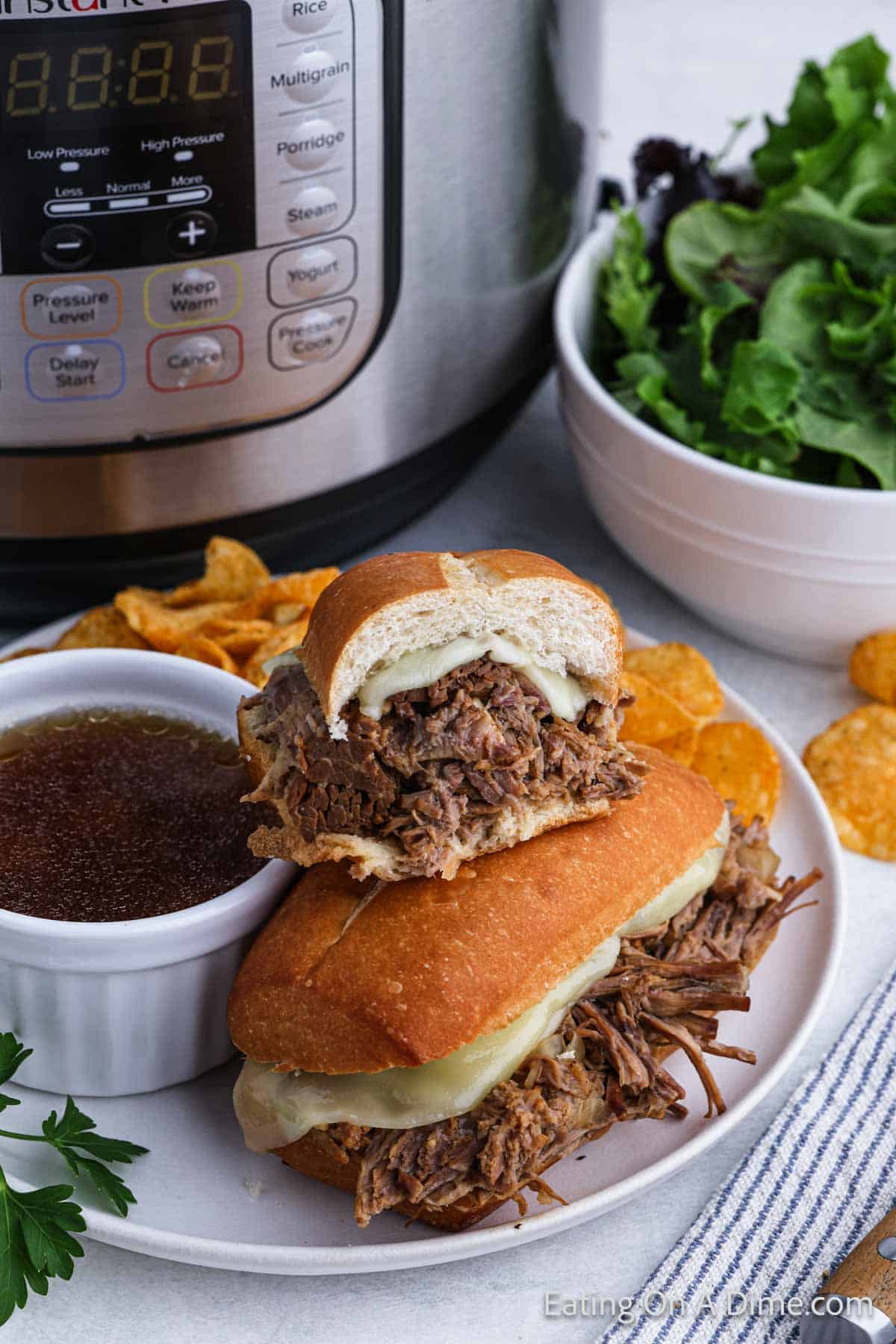 French Dip Sandwiches stacked on a plate with chips and au jus sauce with an instant pot in the background