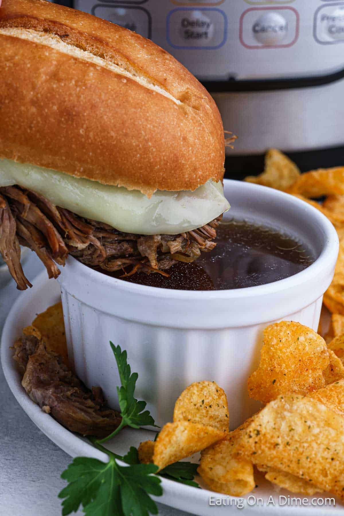 French Dip Sandwich being dipped into a bowl of au jus with a side of chips
