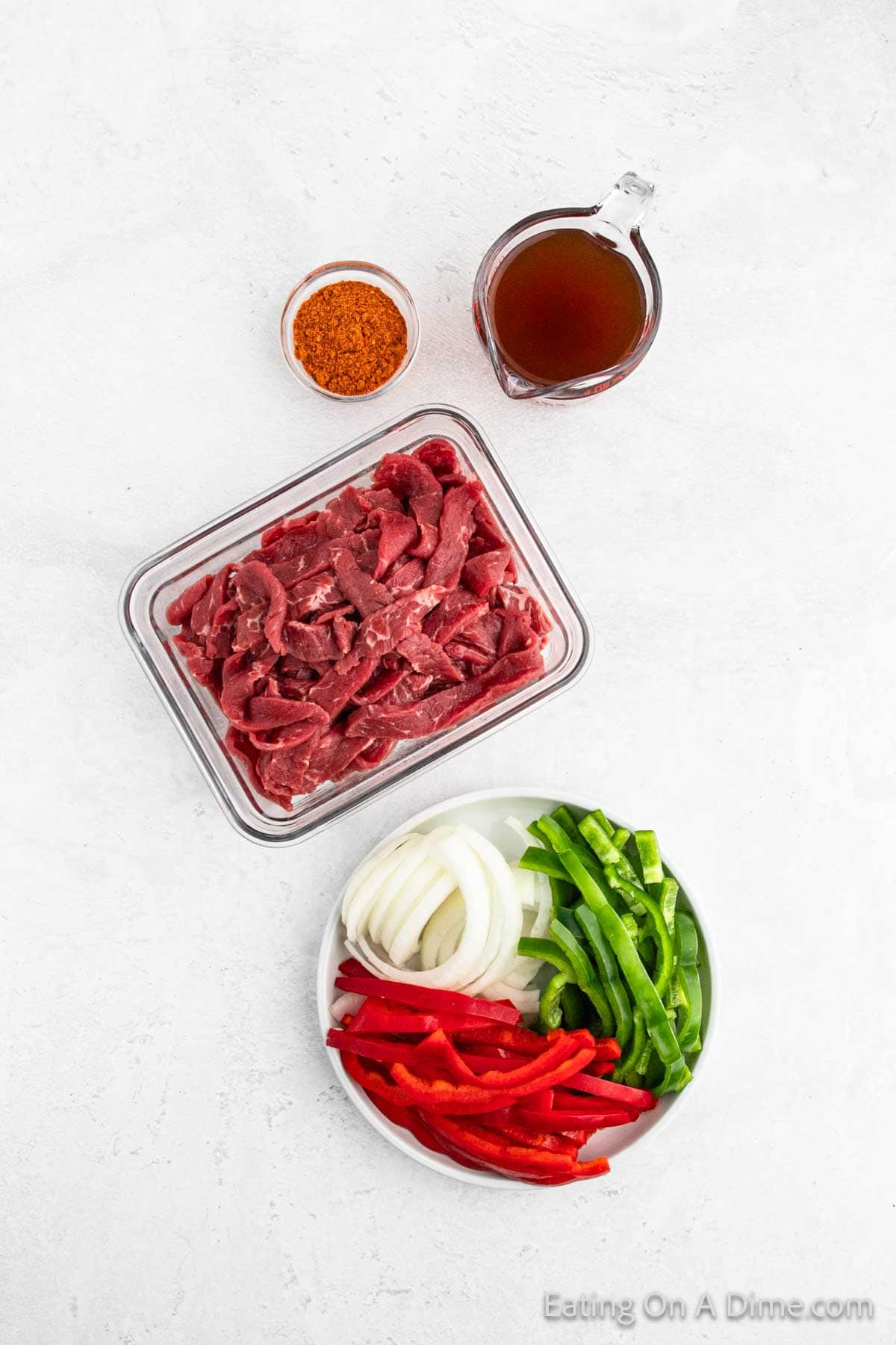 Ingredients - Strips of steak, taco seasoning, bell peppers and onions with a bowl of beef broth