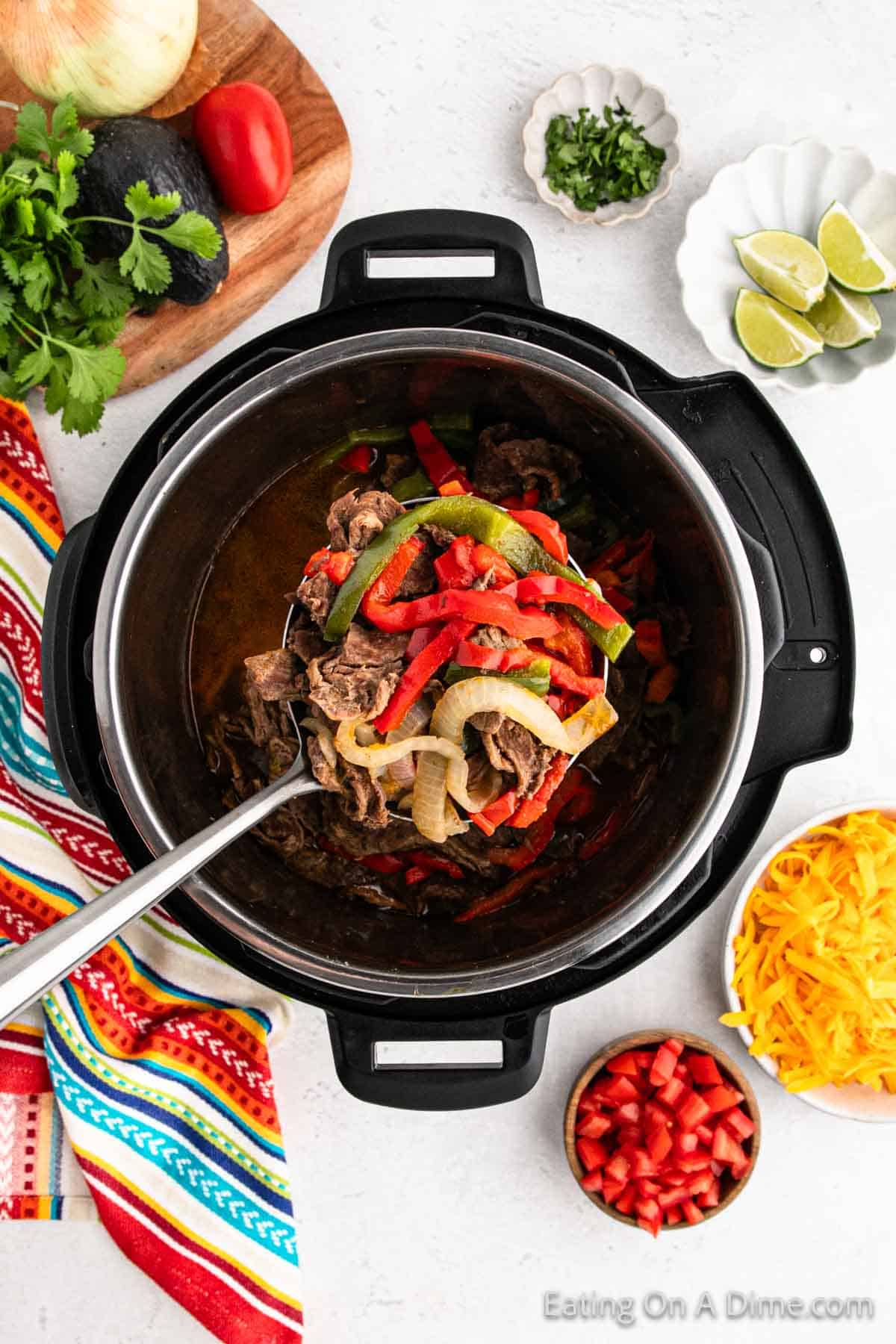 A serving of steak fajitas on a large spoon with red and green bell peppers in the instant pot