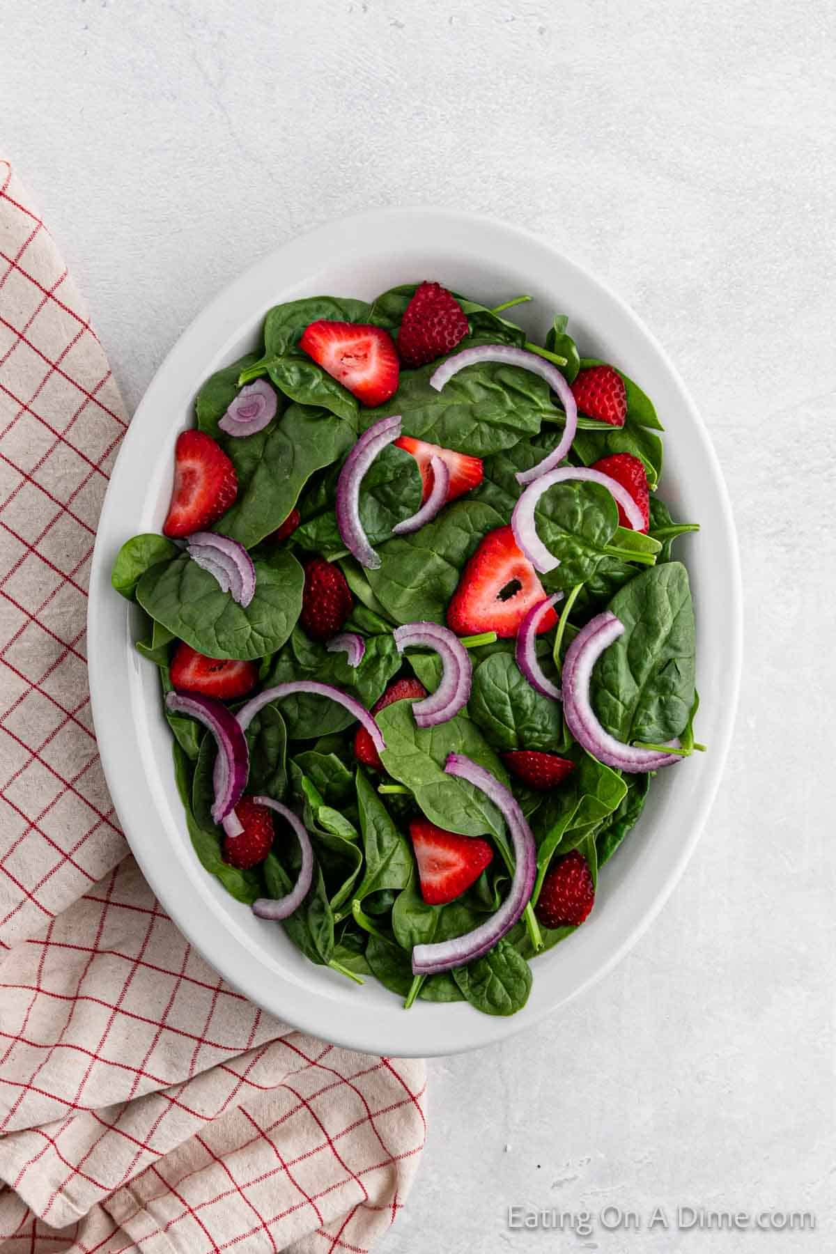 Fresh spinach topped with slice strawberries and red onion