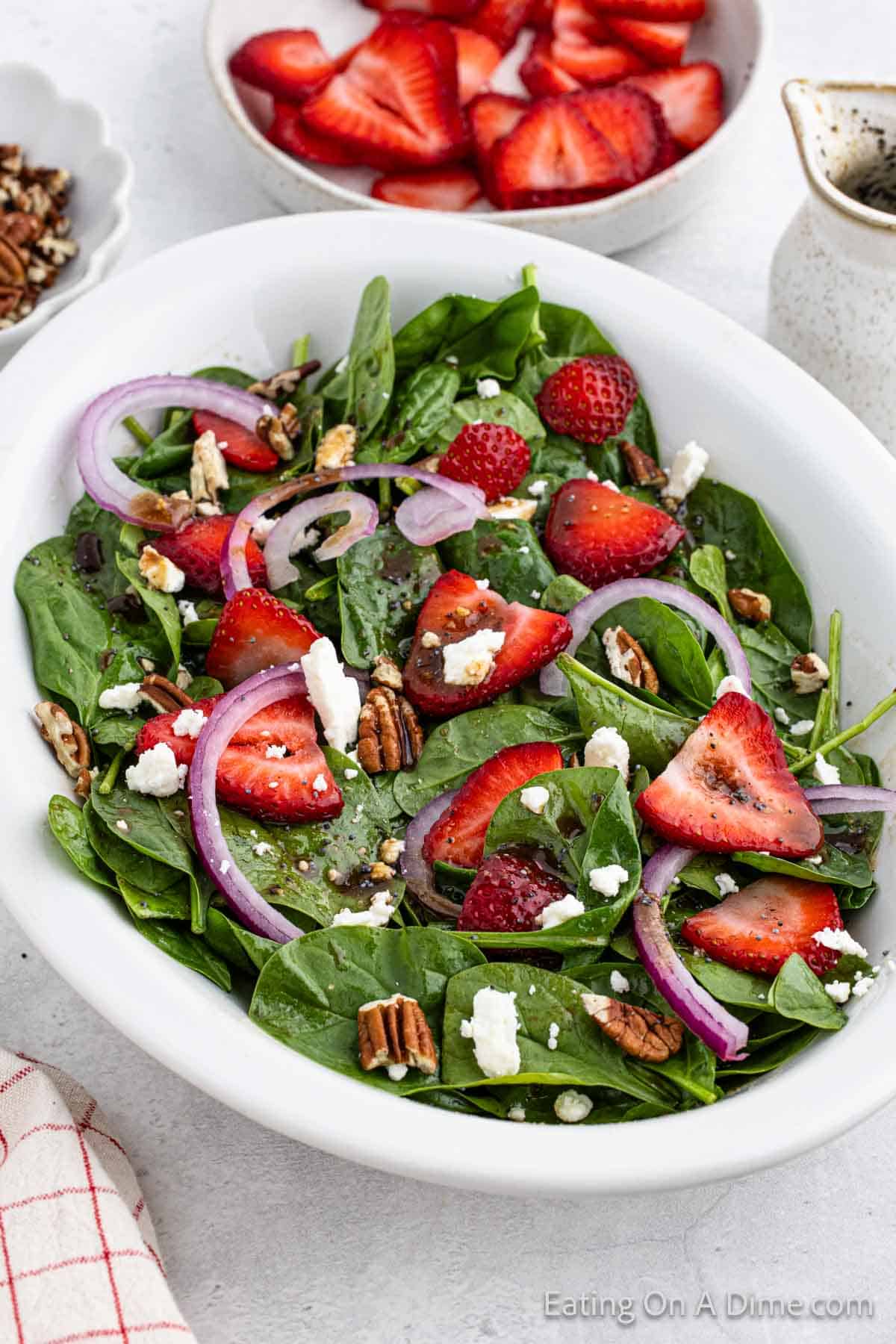 Strawberry Spinach Salad in a white bowl topped with slice strawberries and red onions