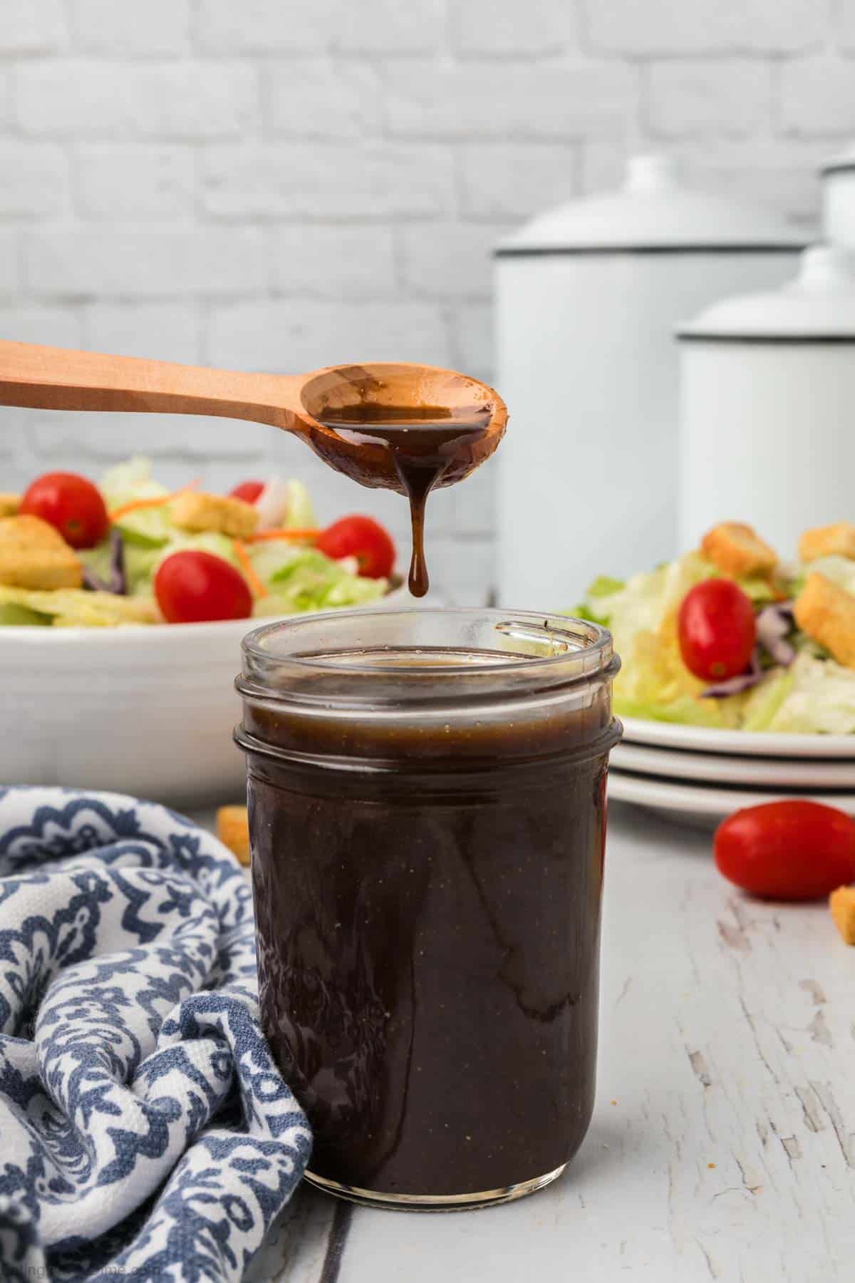 Balsamic Vinaigrette Dressing in a mason jar with a serving on a wooden spoon with a green salad in the background