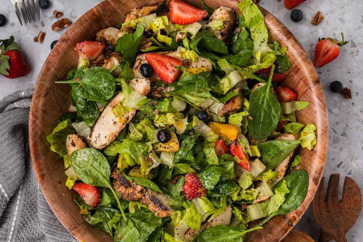 Strawberry Poppyseed Salad in a large brown bowl topped with slices of grilled chicken, slice strawberries, blueberries and oranges