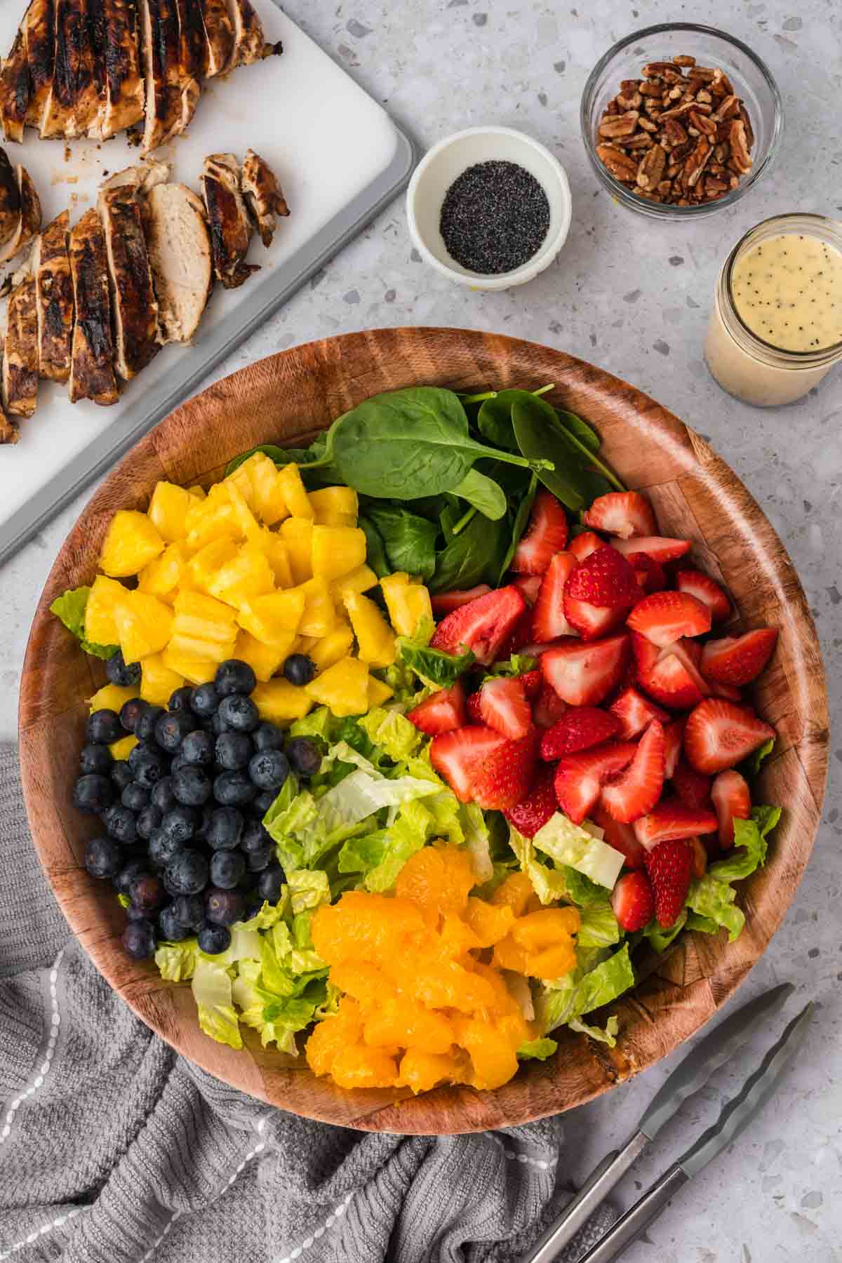 Brown bowl with chopped romaine lettuce, spinach, chopped pineapple, blueberries, slice strawberries and mandarin oranges