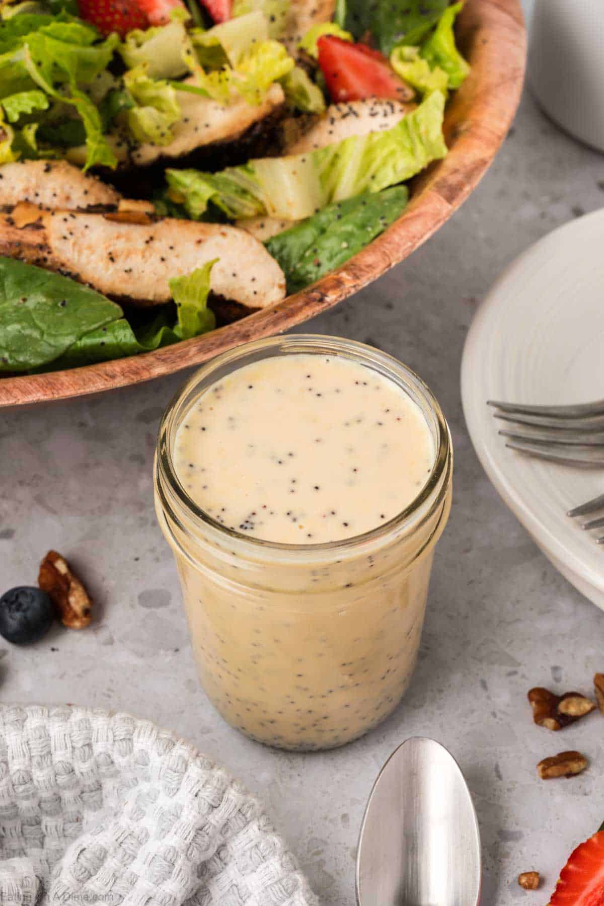 Poppyseed salad dressing in a jar with chicken salad in a wooden bowl 