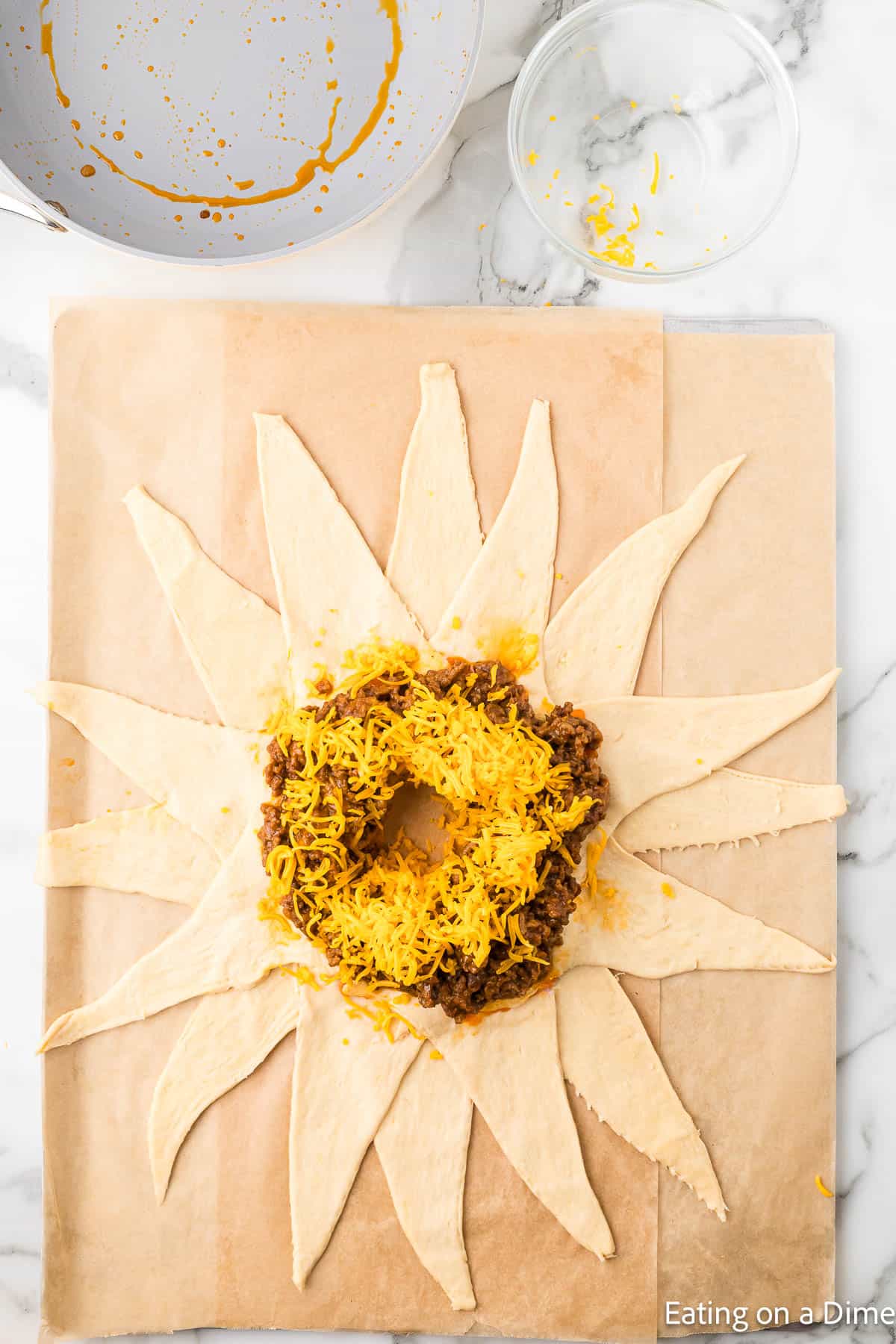 Crescent roll dough on a parchment paper topped with seasoned ground beef and shredded cheese