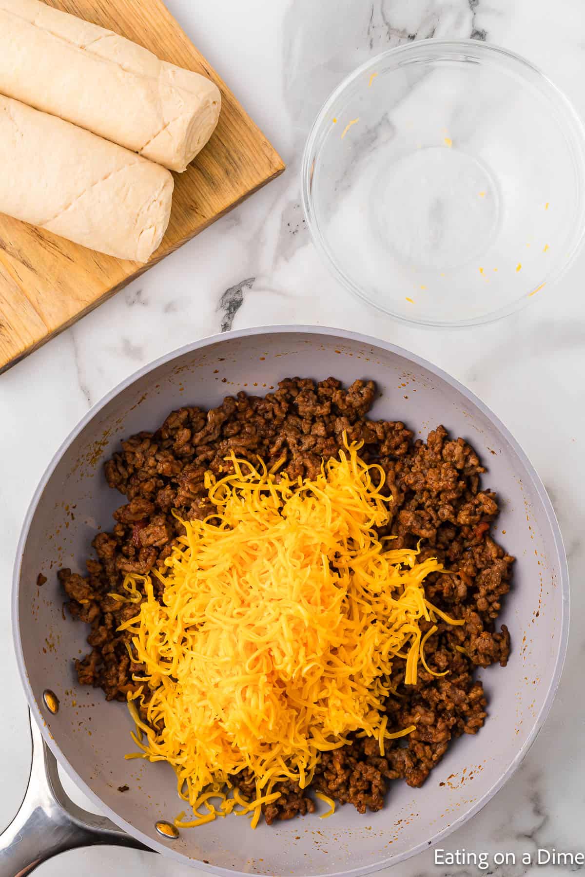 Shredded cheese topped on seasoned ground beef in a large skillet