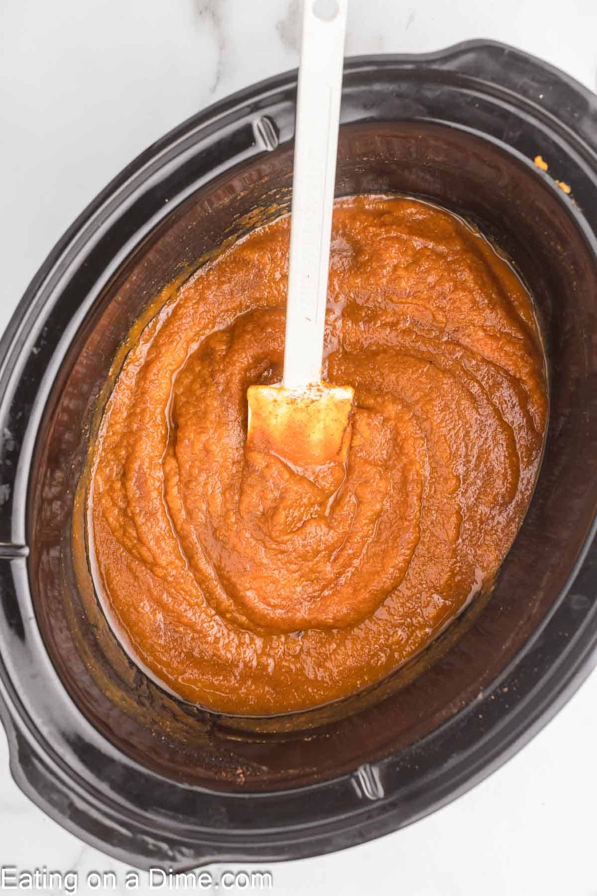 Pumpkin butter in the slow cooker with a white spatula