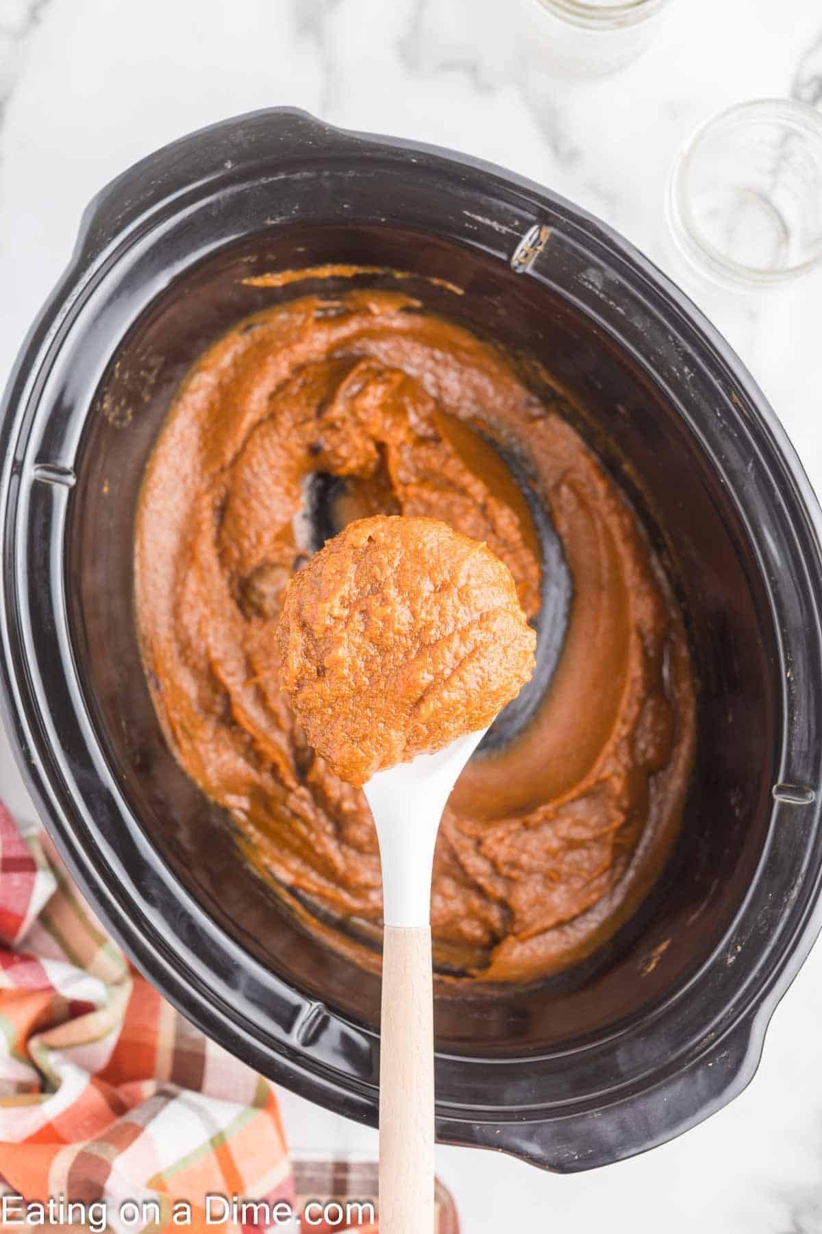 Pumpkin butter in the slow cooker with a serving on a white spoon