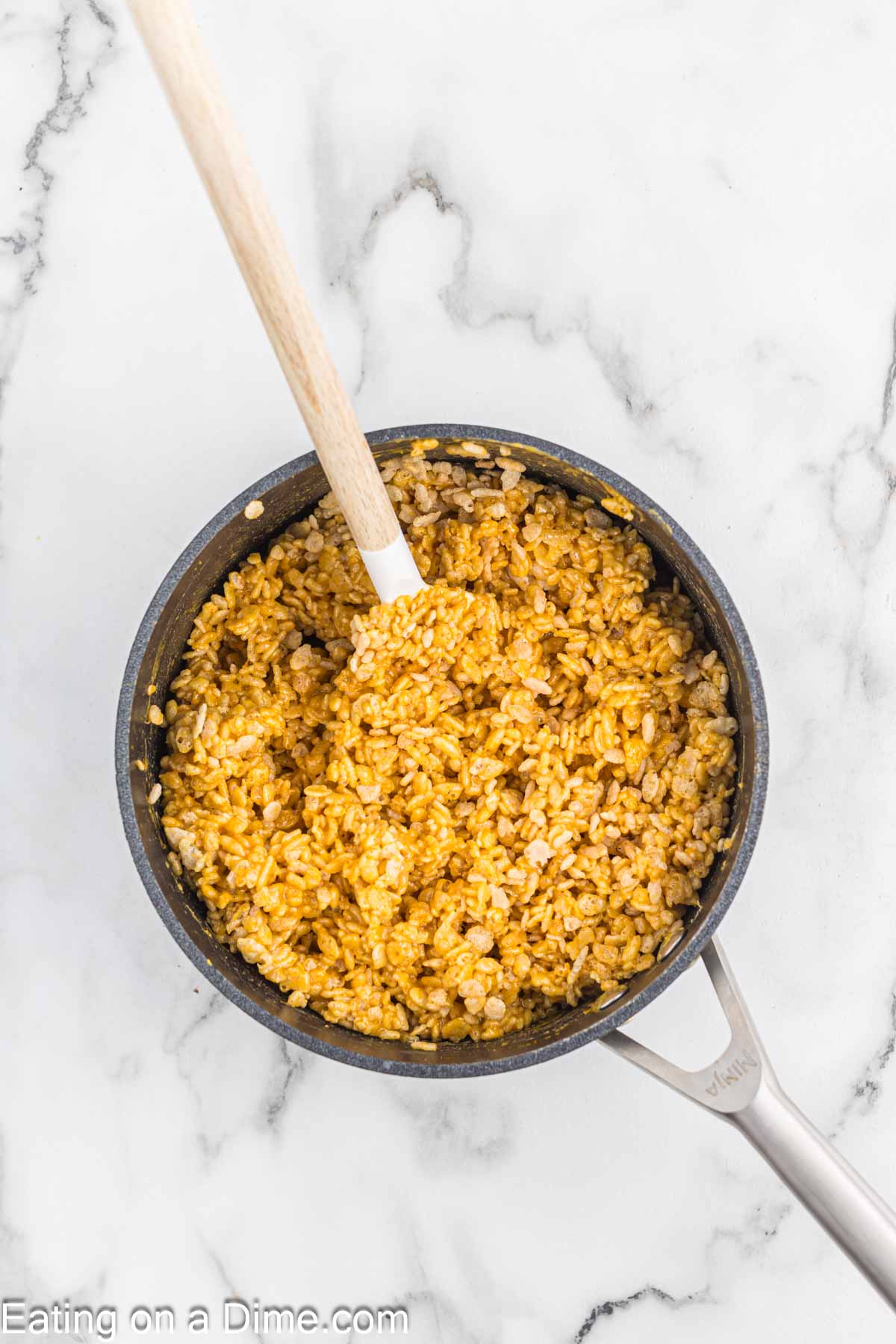 A pot of seasoned rice with a wooden spoon on a marble countertop. The rice, reminiscent of pumpkin rice krispie treats, appears well-cooked and mixed with spices, giving it a rich, golden-brown color.