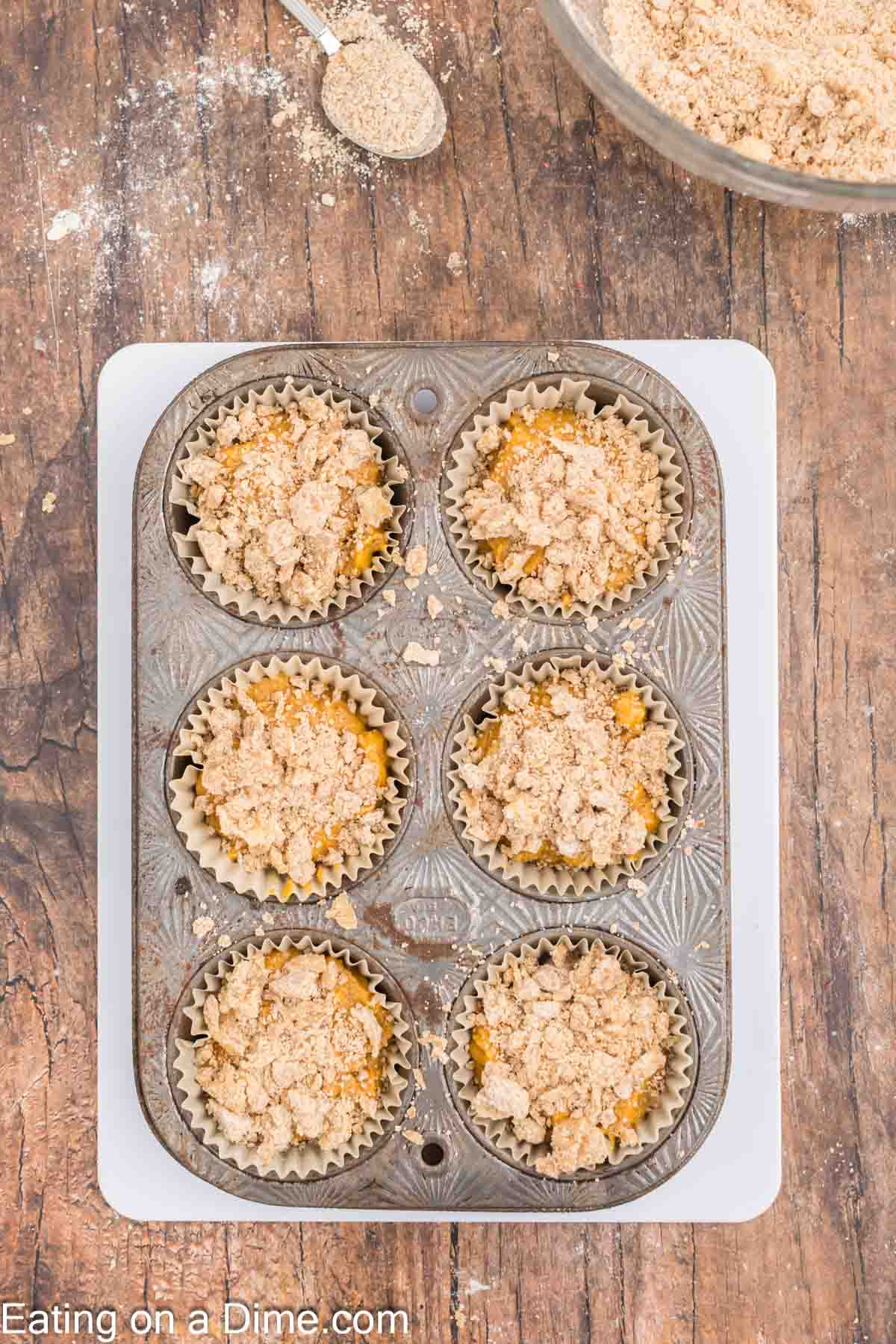 Pumpkin batter placed in muffin tin topped with streusel ready to bake