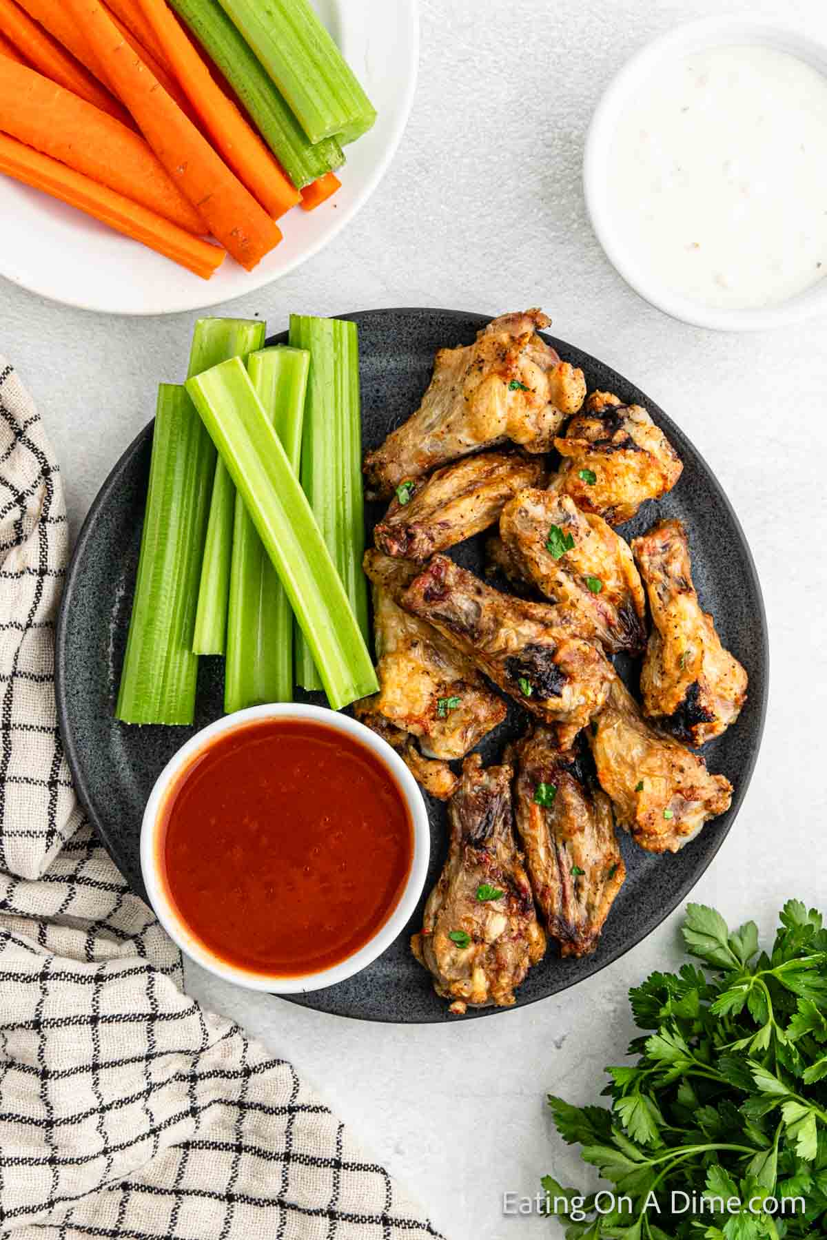 Chicken wings on a plate with celery sticks and a bowl of buffalo sauce