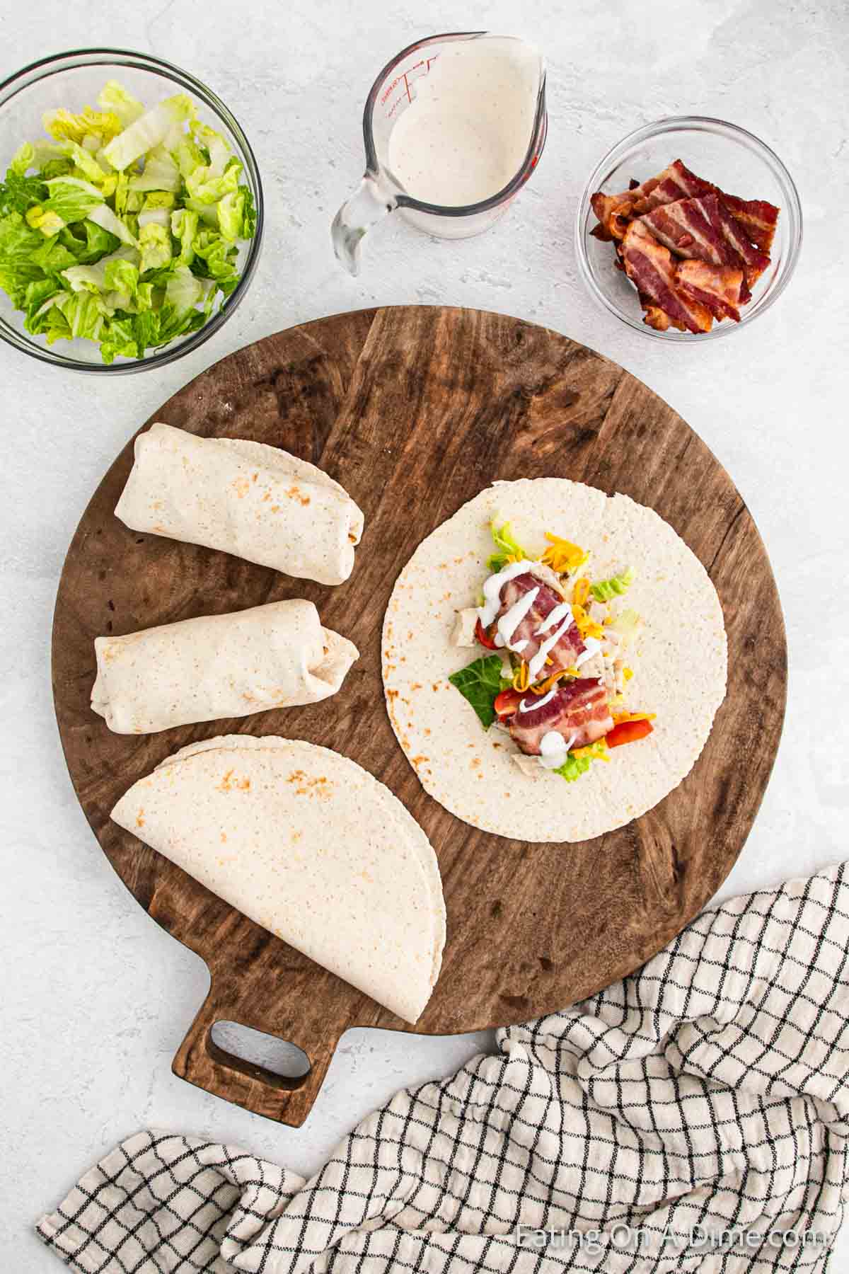 Bowl of shredded lettuce, ranch bacon, and wraps on a cutting board
