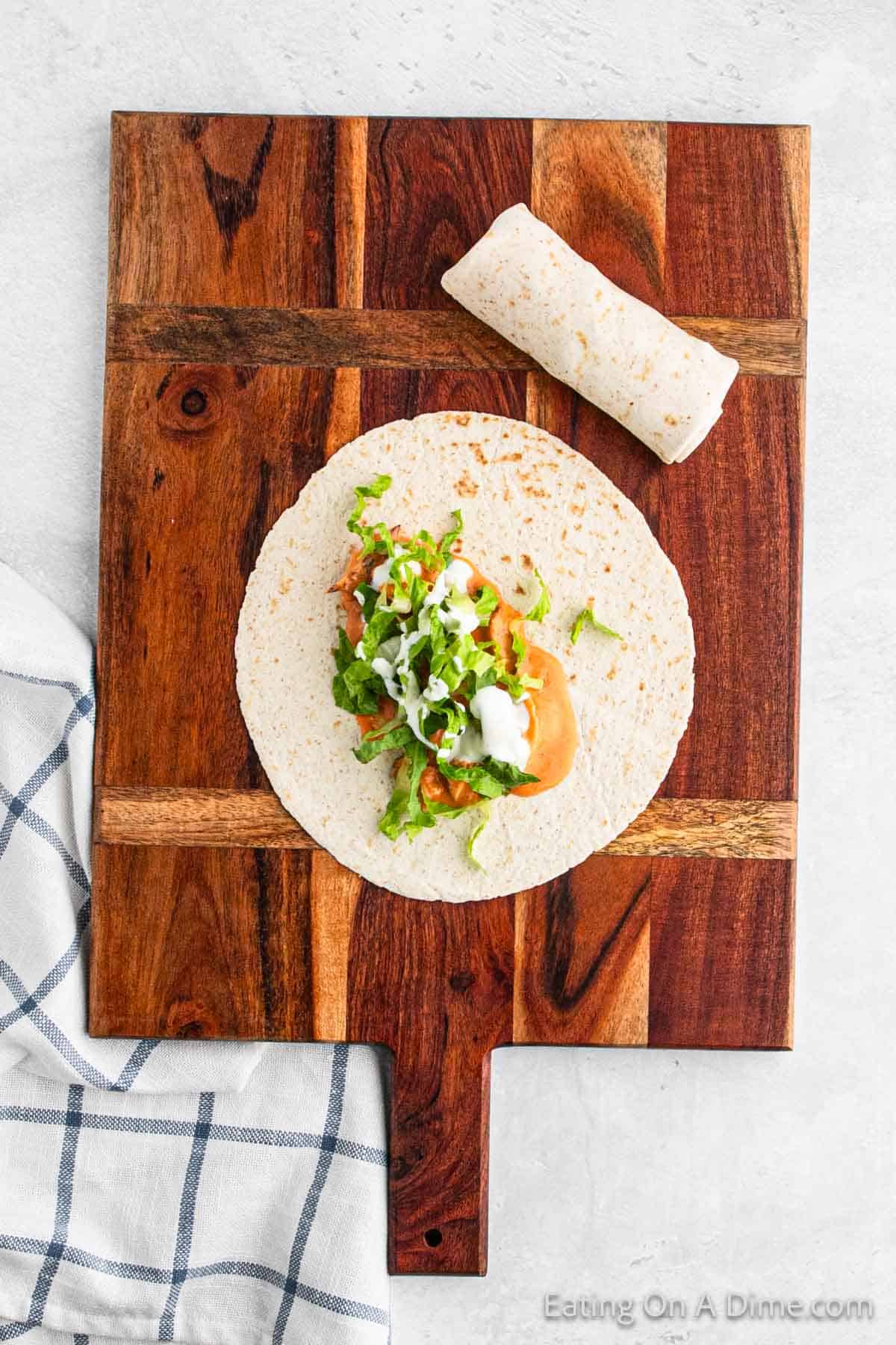 Tortilla on a cutting board topped with buffalo sauce chicken and lettuce
