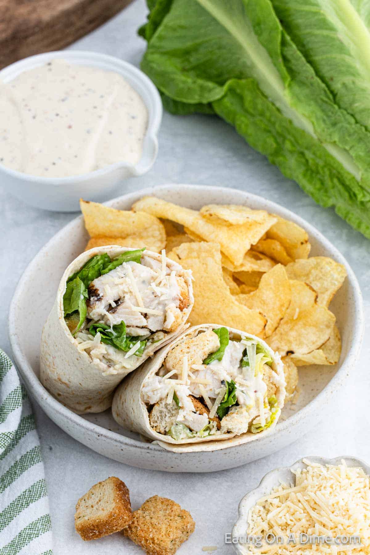Chicken caesar wrap cut in half on a plate with chips