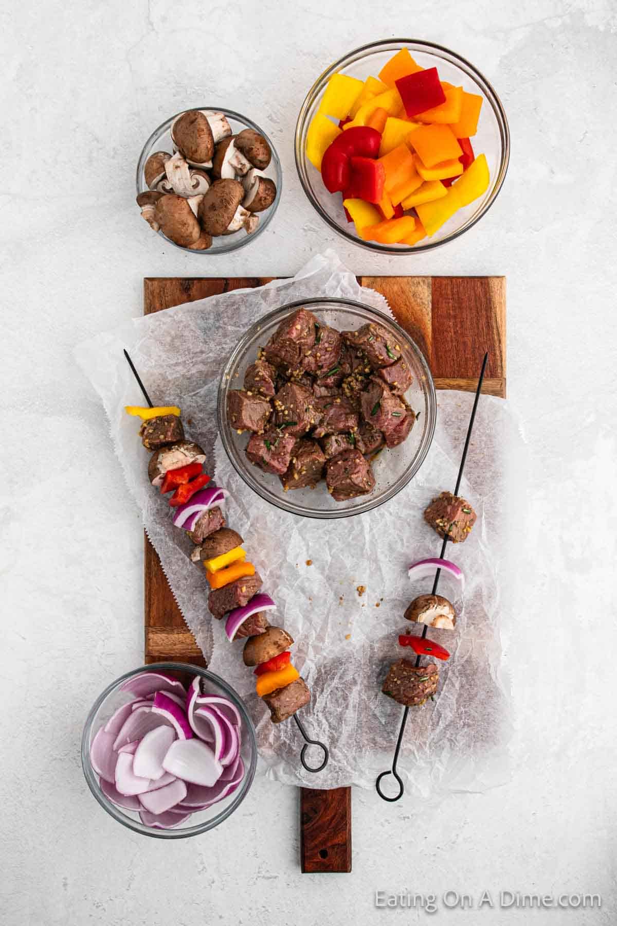 Steak kabobs on a cutting board with bowls of steak and veggies on the side