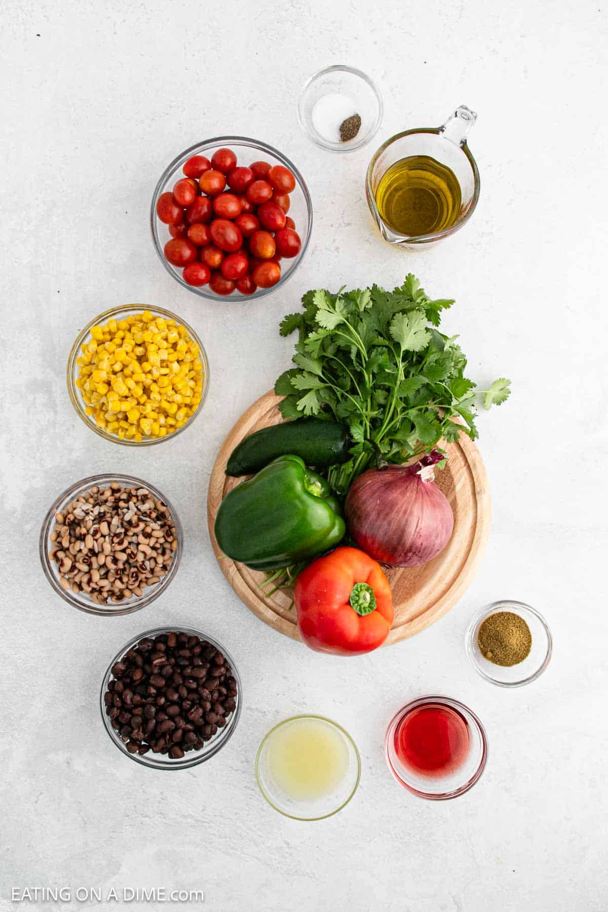 A vibrant array of ingredients for Texas caviar is artfully arranged: cherry tomatoes, corn, black-eyed peas, black beans, green bell peppers, a red pepper, a red onion, jalapeños, cilantro. These are complemented by olive oil, lemon juice, vinegar, cumin and a single spice.