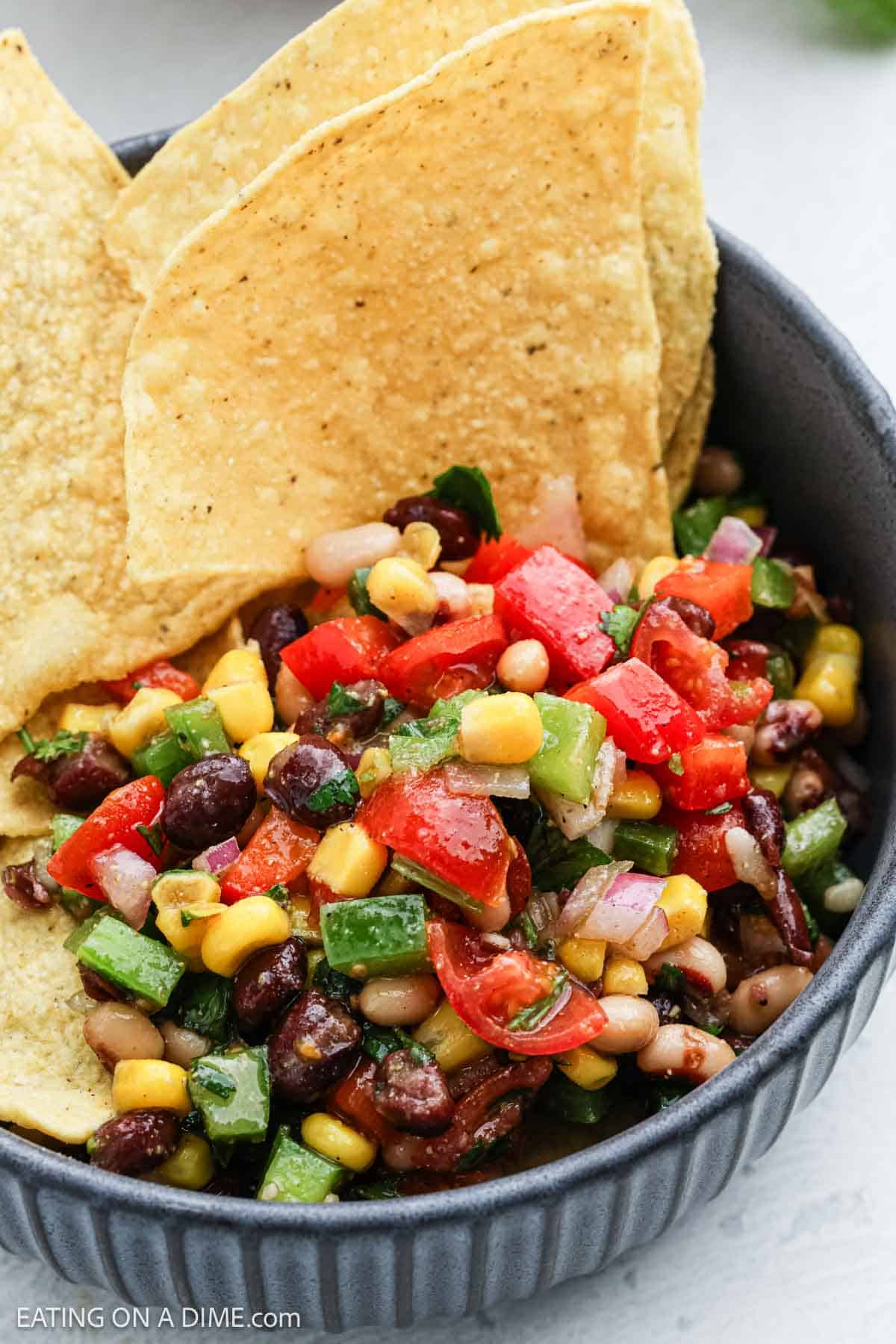 A gray bowl brimming with Texas caviar—a colorful salsa of black beans, corn, diced tomatoes, green peppers, and onions—nicely garnished with crispy tortilla chips.